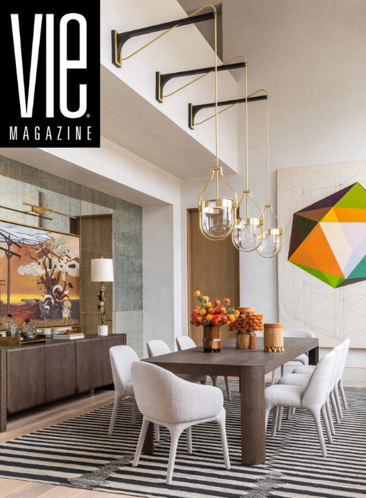 Modern dining room with a wooden table, six upholstered chairs, a striped rug, and decorative arrangements of flowers and candles. Wall art and stylish lighting fixtures are also visible.