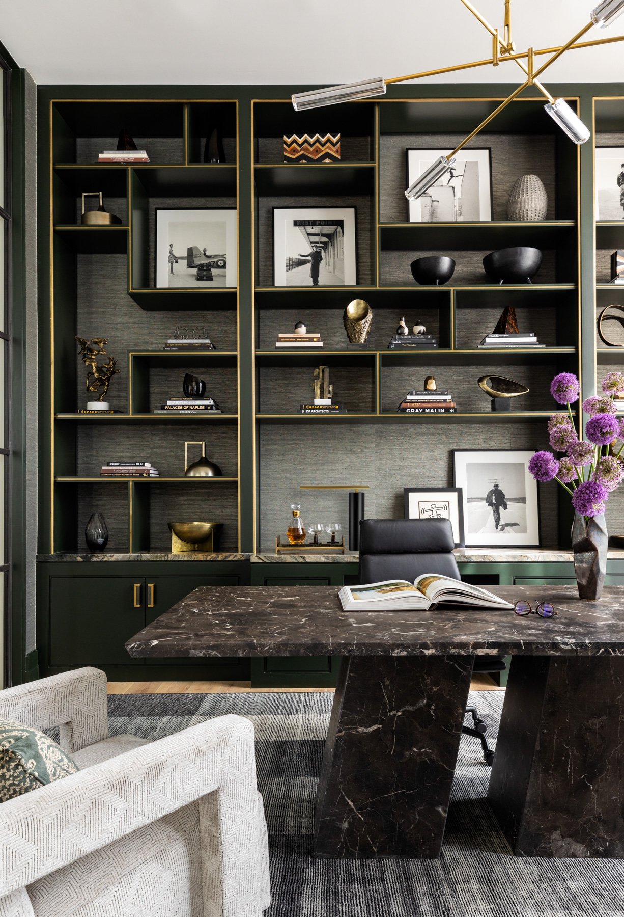Benjamin Johnston Design Houston luxury interior design and architecture — home office detail with black marble desk, dark green built-in shelving with brass trim, and curated art and sculpture collection.
