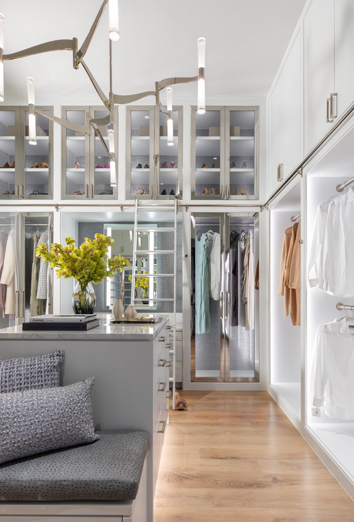 Benjamin Johnston Design Houston luxury interior design and architecture — luxury walk-in closet with floor-to-ceiling glass front cabinetry, marble island, rolling library ladder, nickel hardware, and sculptural nickel chandelier.