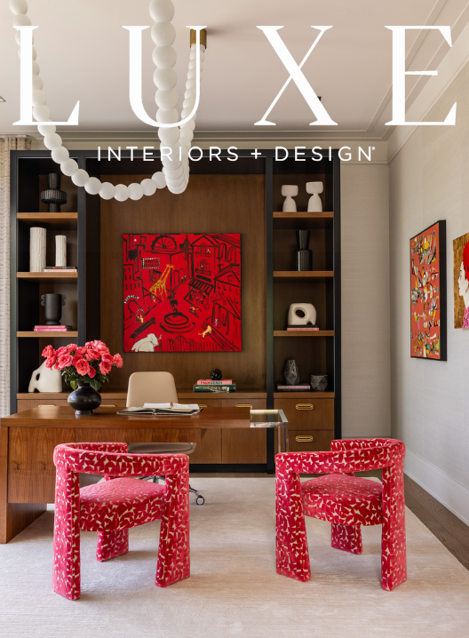 An office with a wooden desk, two red patterned chairs, a built-in dark wood bookshelf with decorative items, and colorful artwork on the walls.