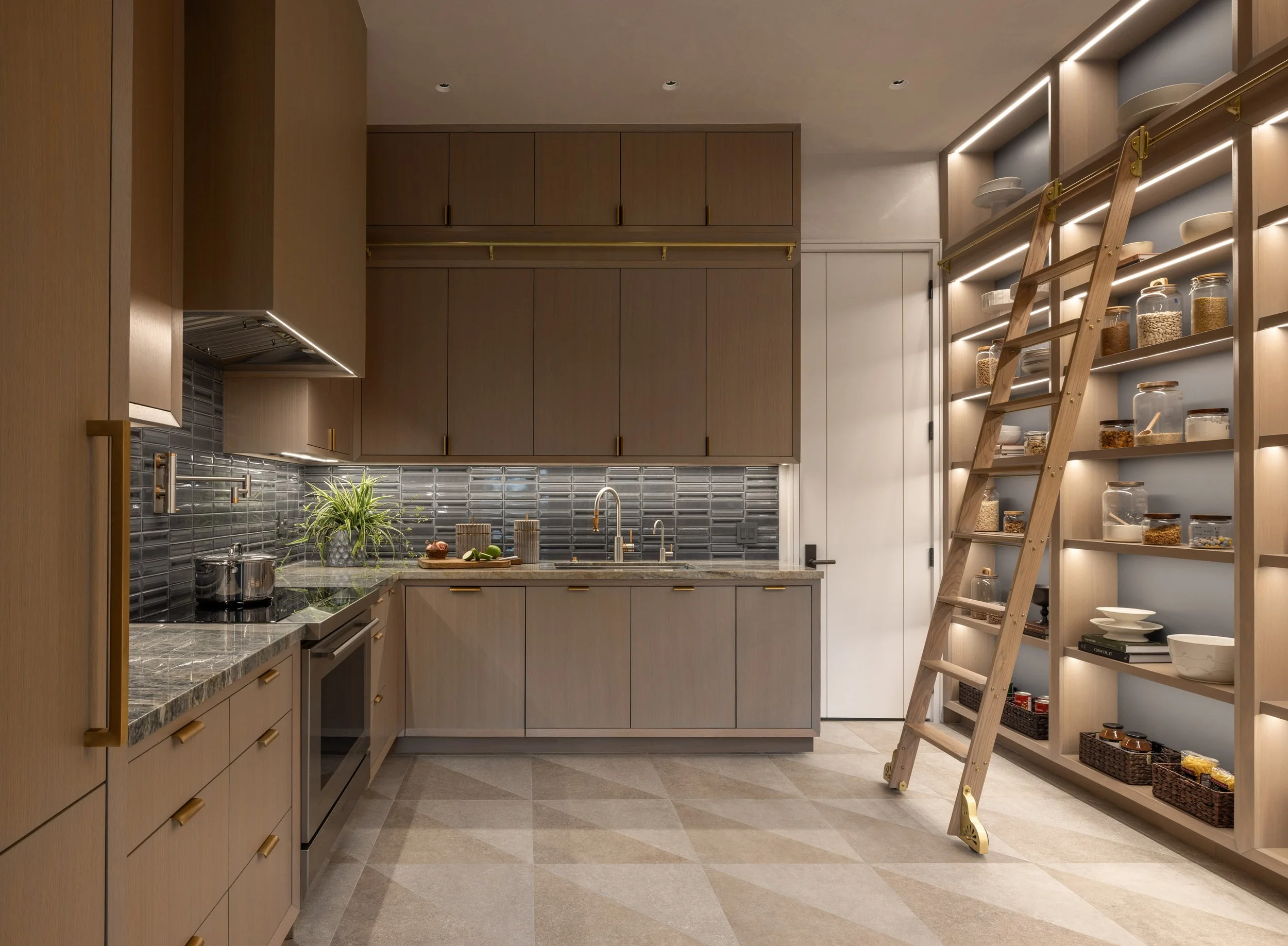 Modern kitchen with wooden cabinets, grey backsplash, marble countertop, and open shelving with jars and dishes. A ladder leans against the shelving, and a small plant is on the counter.