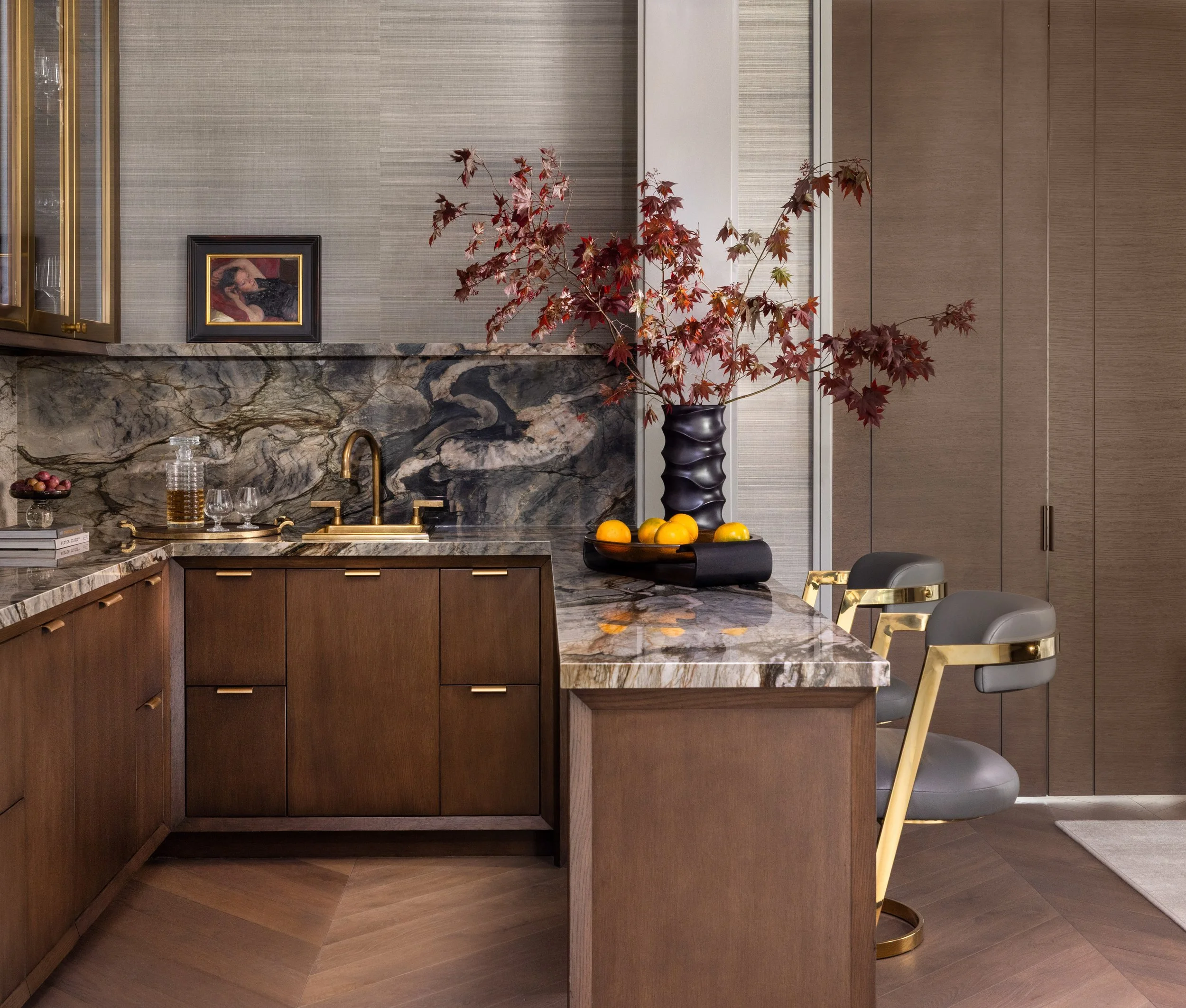 Benjamin Johnston Design Houston home bar detail featuring dramatic veined marble countertop and backsplash, walnut cabinetry with brass hardware, gold bar stool, and Japanese maple branch arrangement.