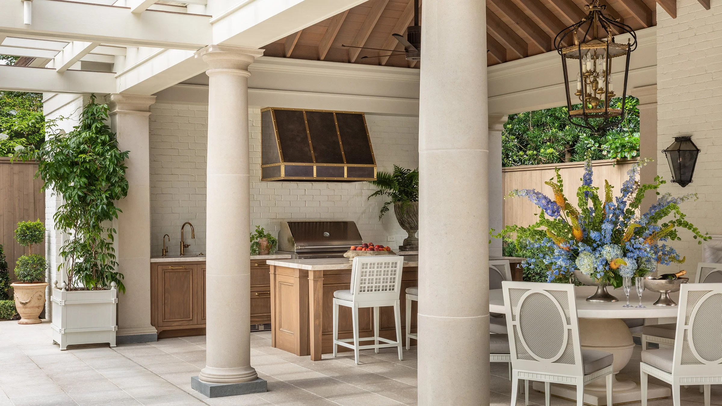 Luxury covered outdoor kitchen with limestone columns, built-in grill, vaulted wood ceiling, and elegant outdoor dining area.