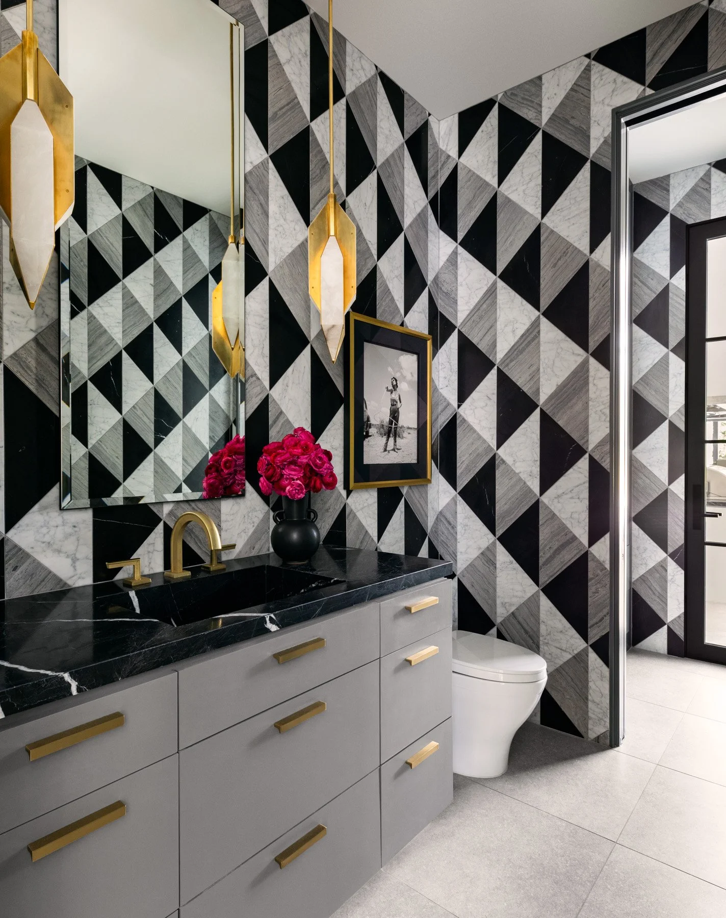 Benjamin Johnston Design Houston luxury residential interior design — luxury pool bath with floor-to-ceiling geometric marble tile, black marble countertop, gray custom vanity, brass hardware, and gold crystal pendant lighting.