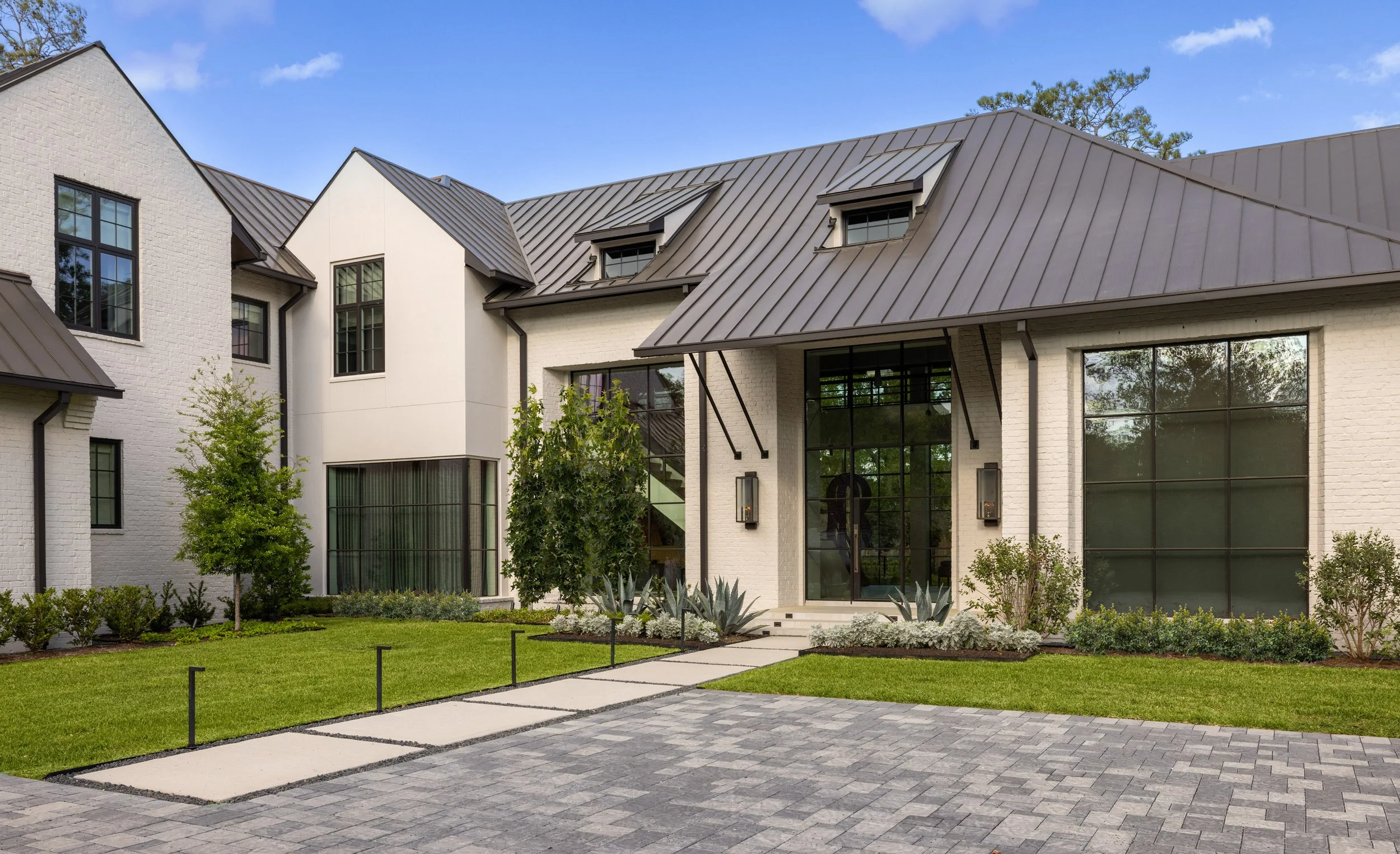 Benjamin Johnston Design residential architecture exterior featuring white brick facade, standing seam metal roof, floor-to-ceiling steel windows, modern entry with stone walkway, and manicured landscaping.