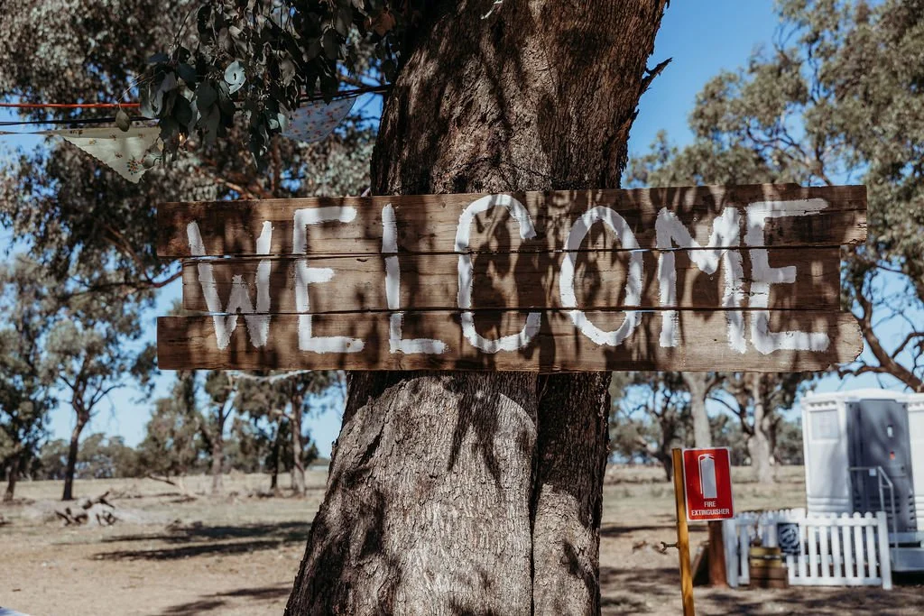 Rustic wooden welcome sign for wedding in a rural setting.