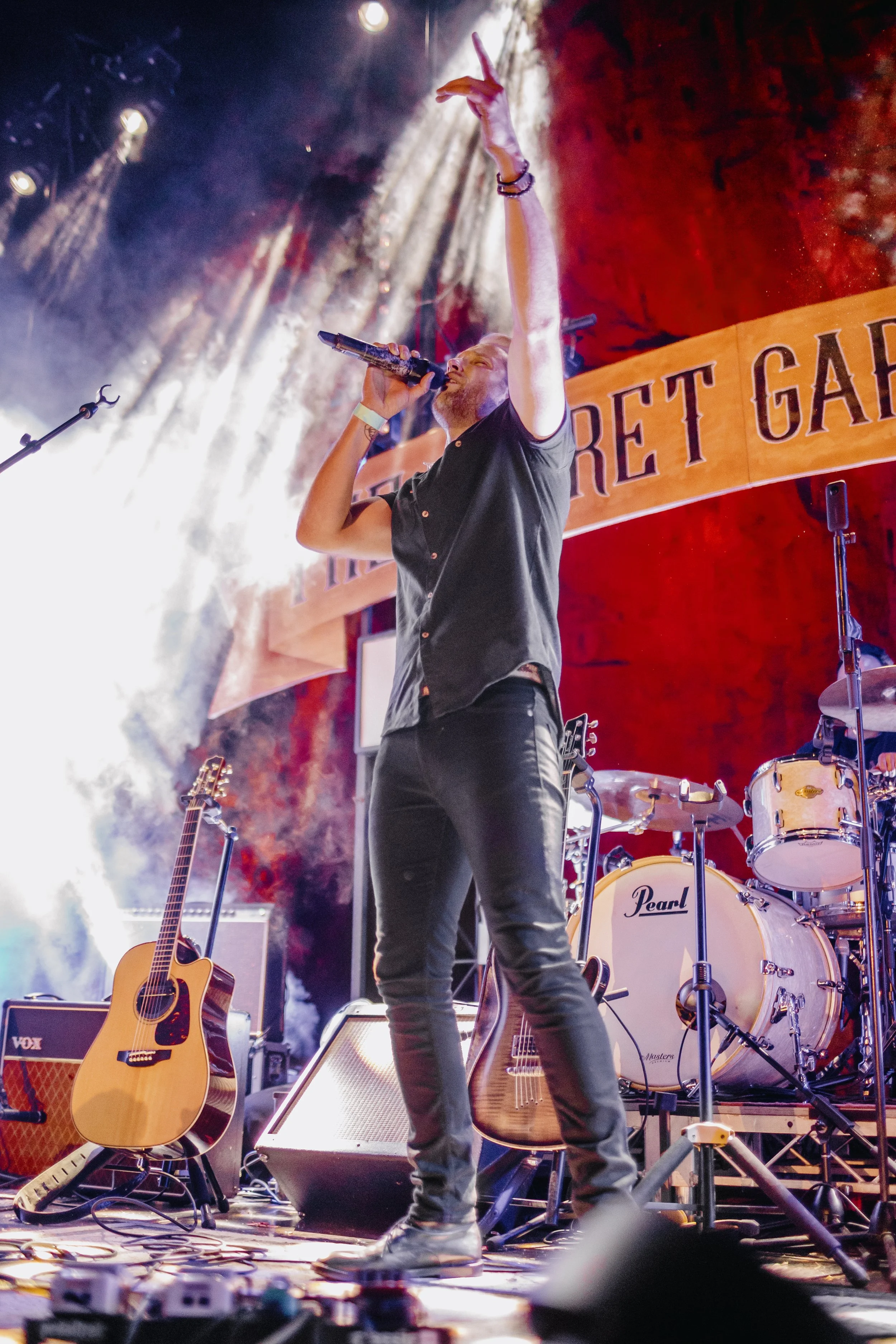 A man singing, raises his hand in the air to encourage the audience.
