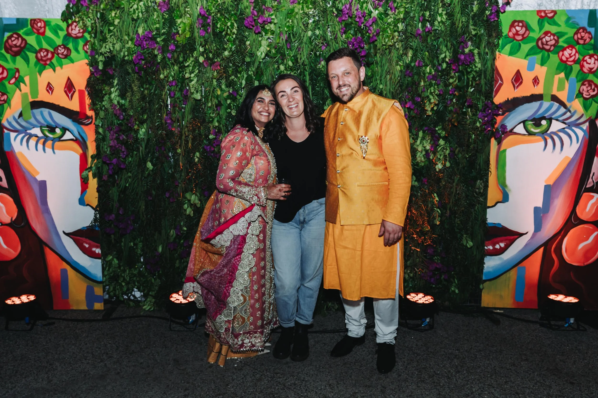 Two people in traditional clothing pose for a photo with a woman in a colorful dress.
