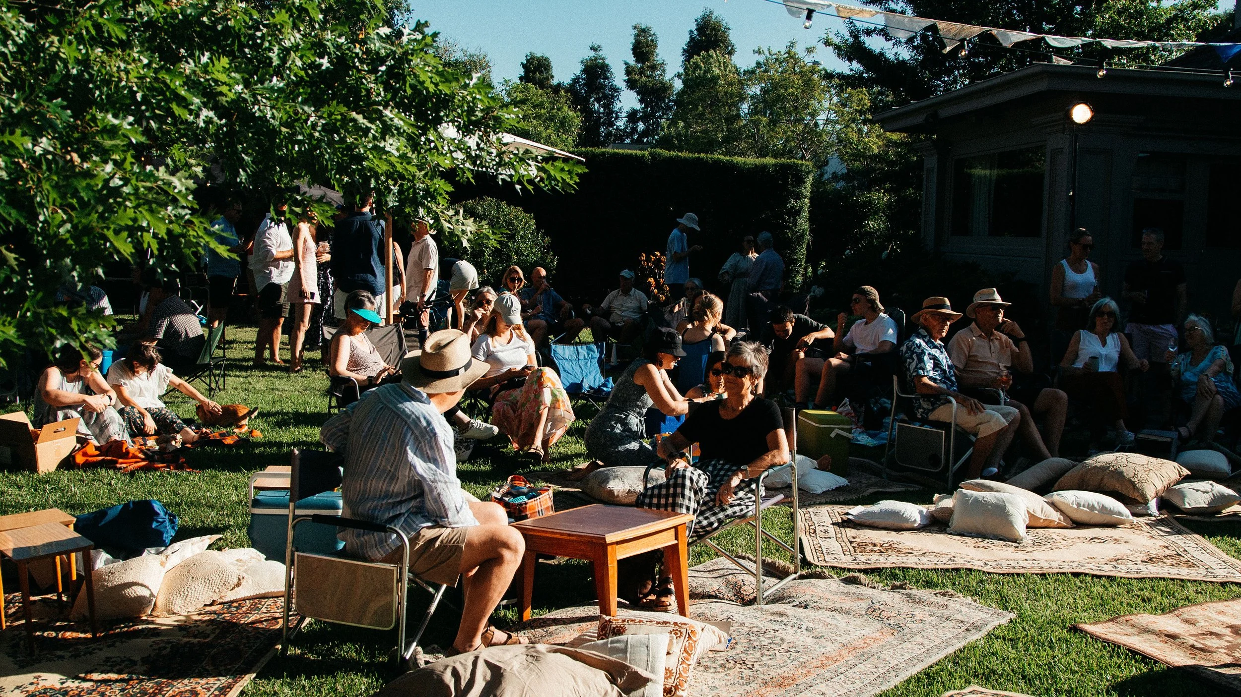 A diverse group of individuals sitting on blankets in the lush green grass, enjoying each other's company.