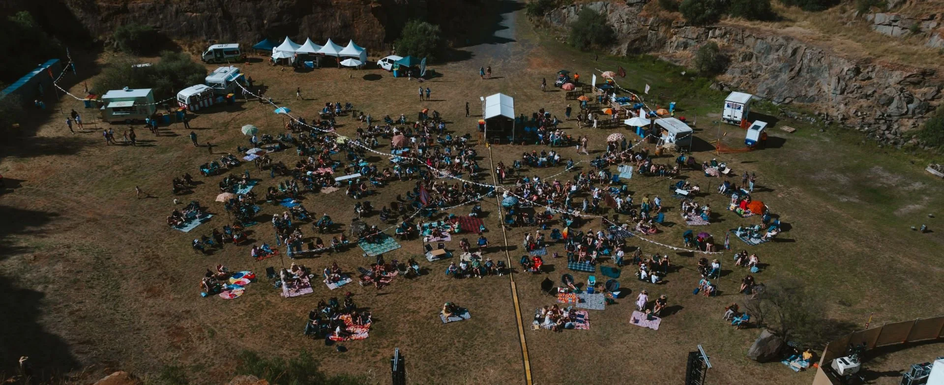 A large crowd gathered around a tent, seen from above at a music festival.