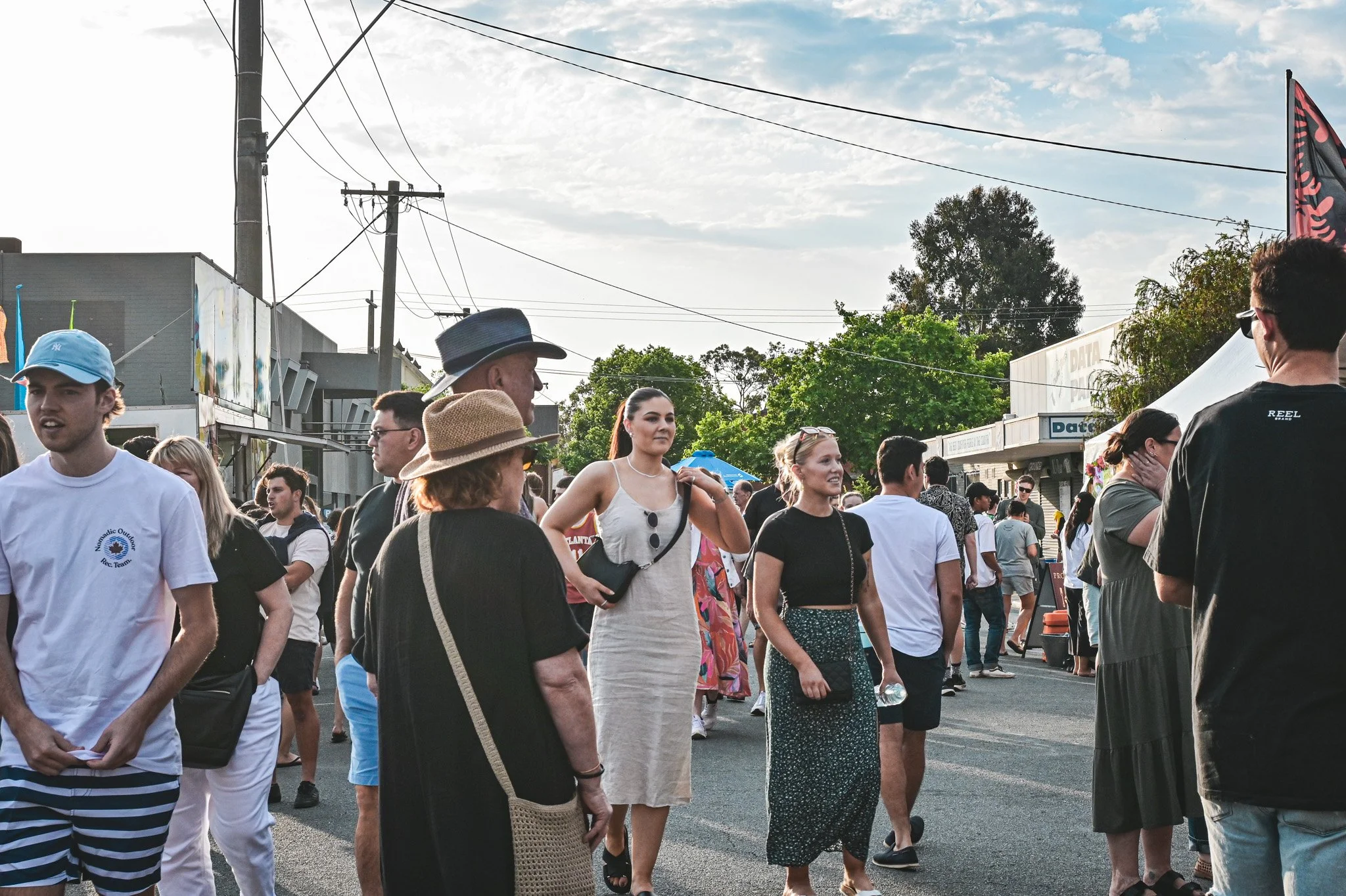 A bustling outdoor market during a food festival, with a lively crowd of people walking down the street.