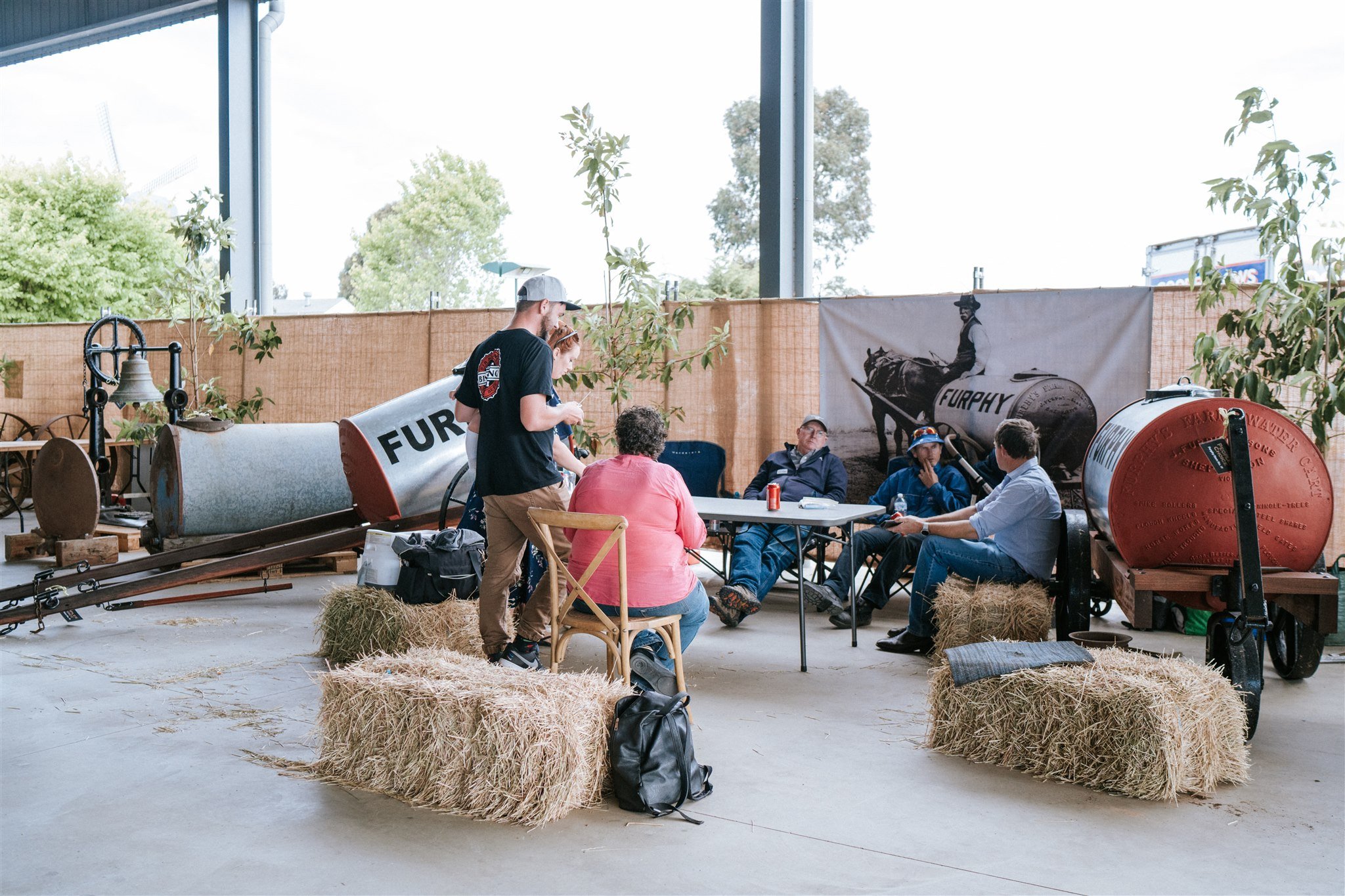 Group of people sitting around a table with hay bales at Furphy 150 Year Celebration.
