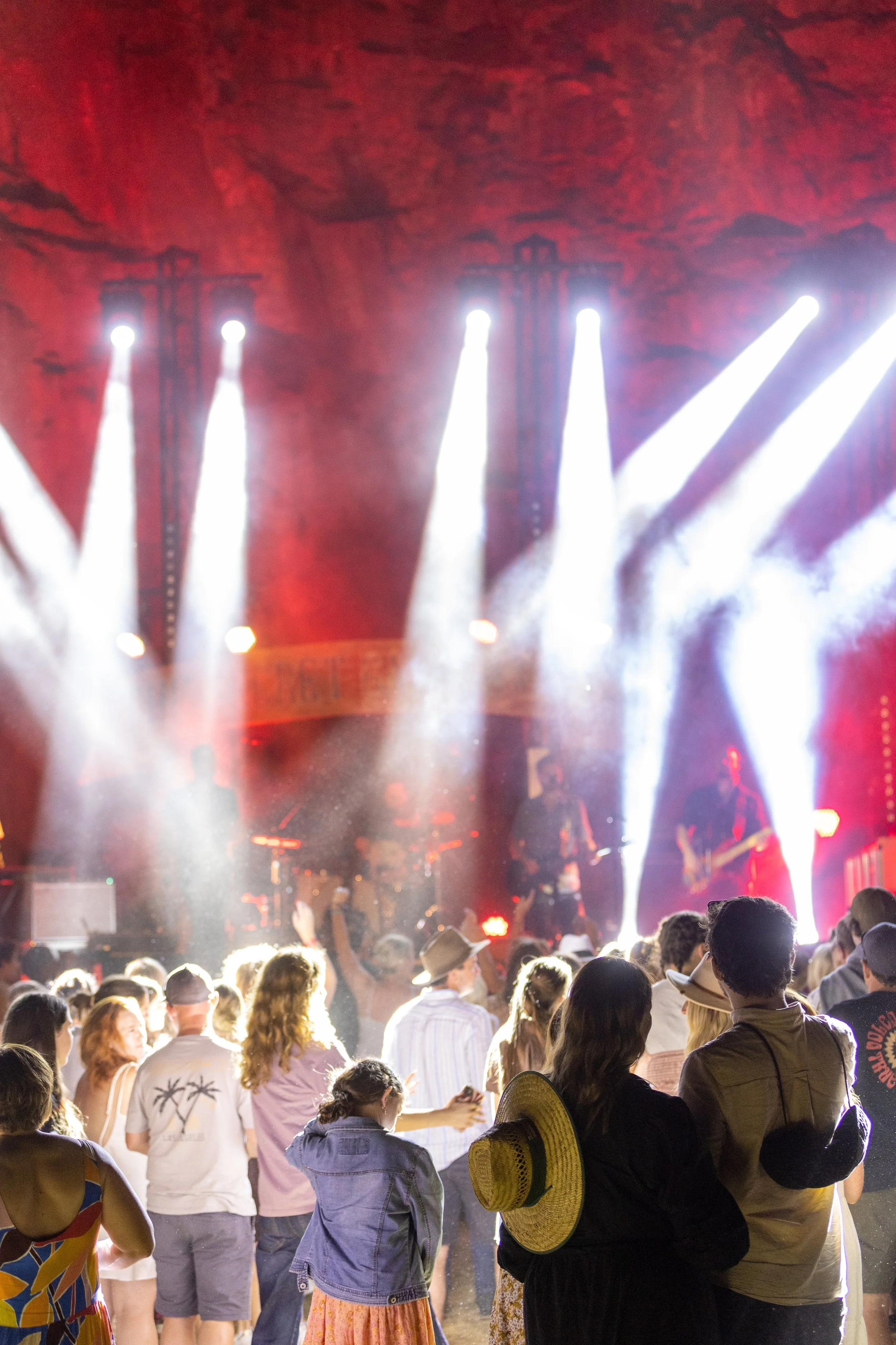 The crowd stands infront of the stage with lots of spotlights.