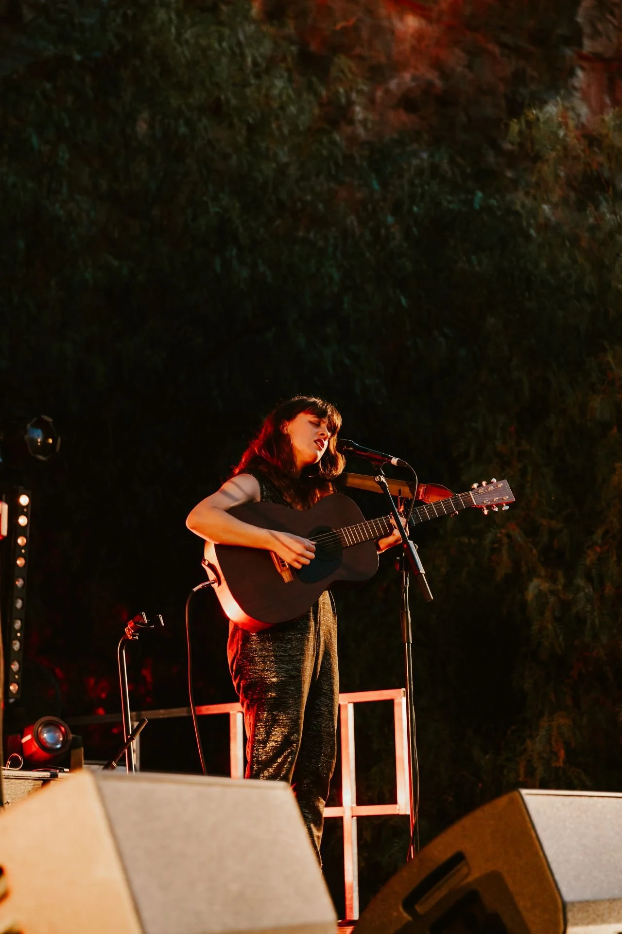 Amidst the enchanting ambiance of a music festival, a woman captivates the audience with her guitar skills on a dimly lit stage at night.