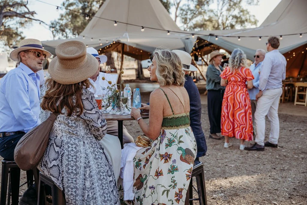 Wedding guests mingling outdoors with spacious tents and greenery in a countryside setting.