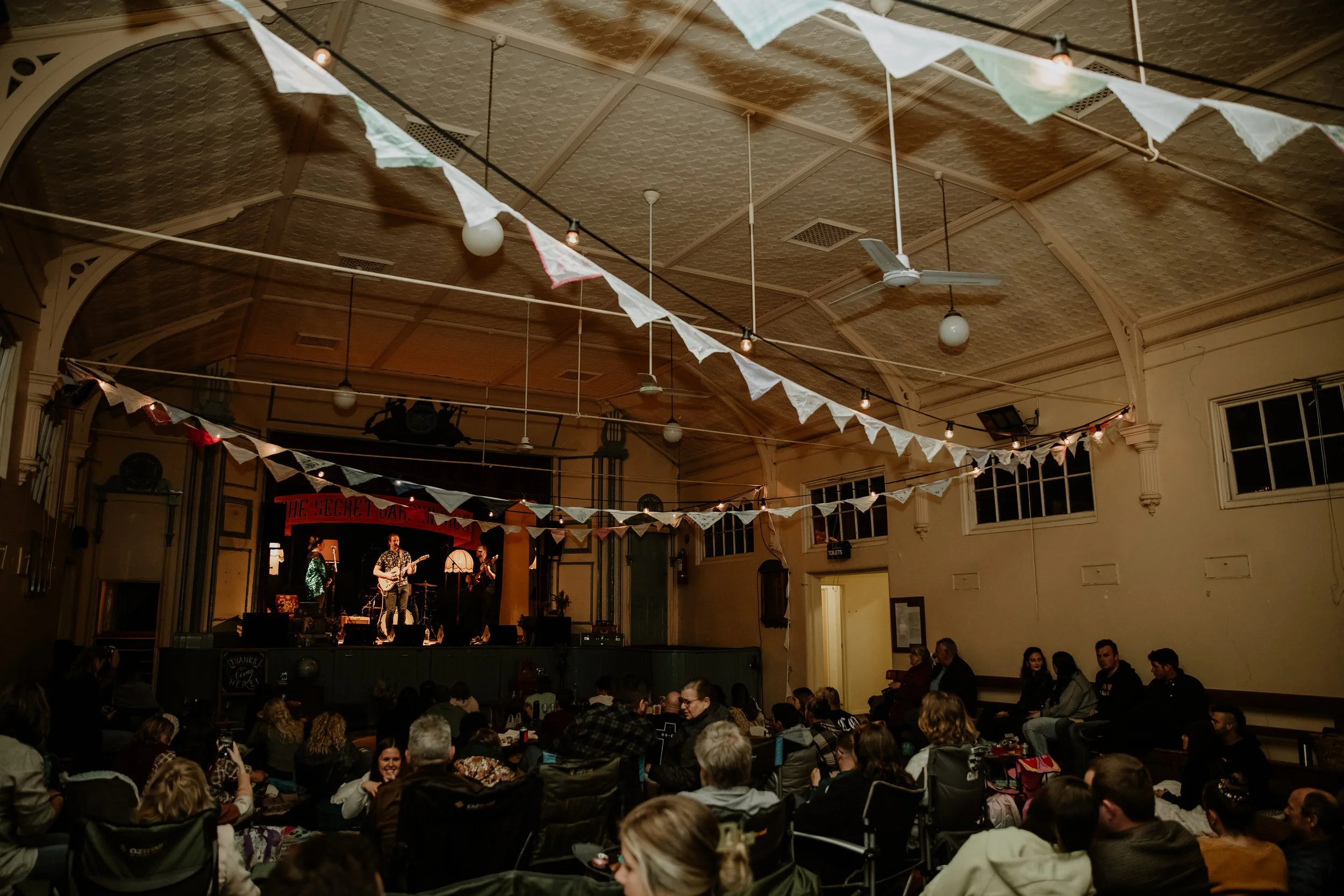A view of the hall with people sitting in camper chairs while enjoying music.