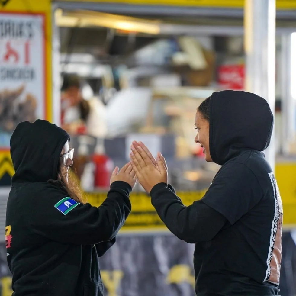 Two women in black hoodies high-fiving each other at Treaty Day Out event.