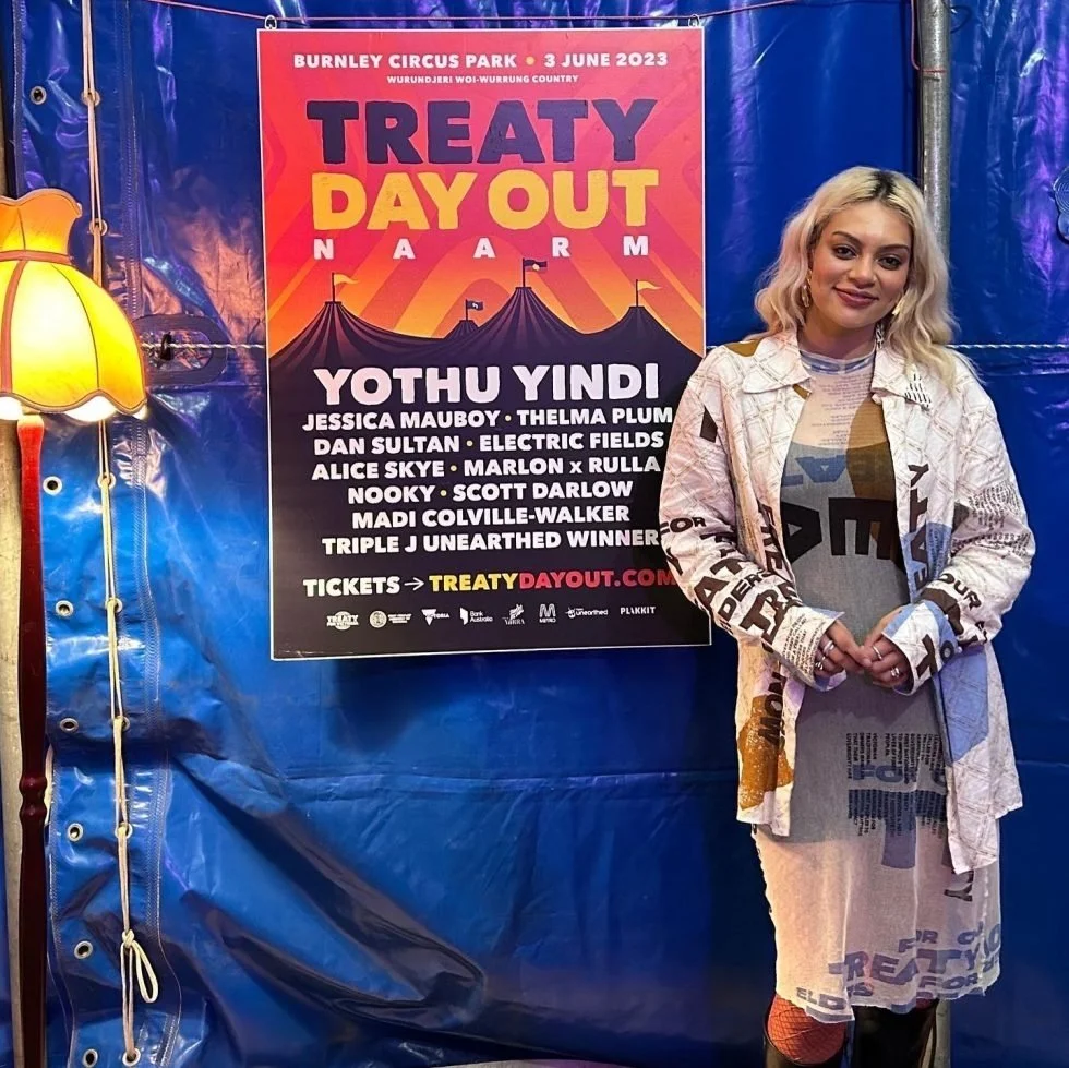 Thelma Plum posing beside a "Treaty Day Out" festival poster.