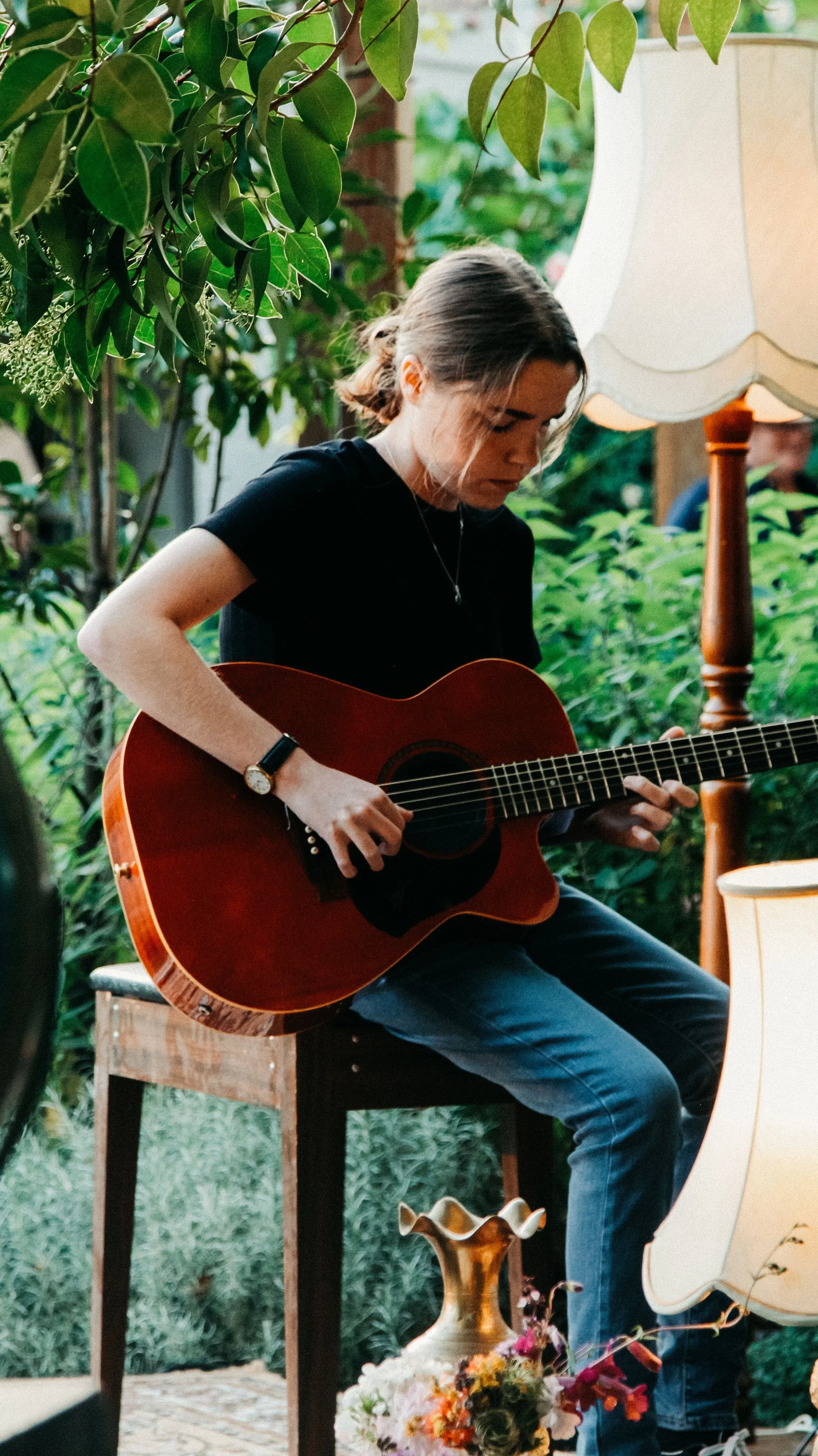 Guitarist performing with an acoustic guitar in a lush garden.