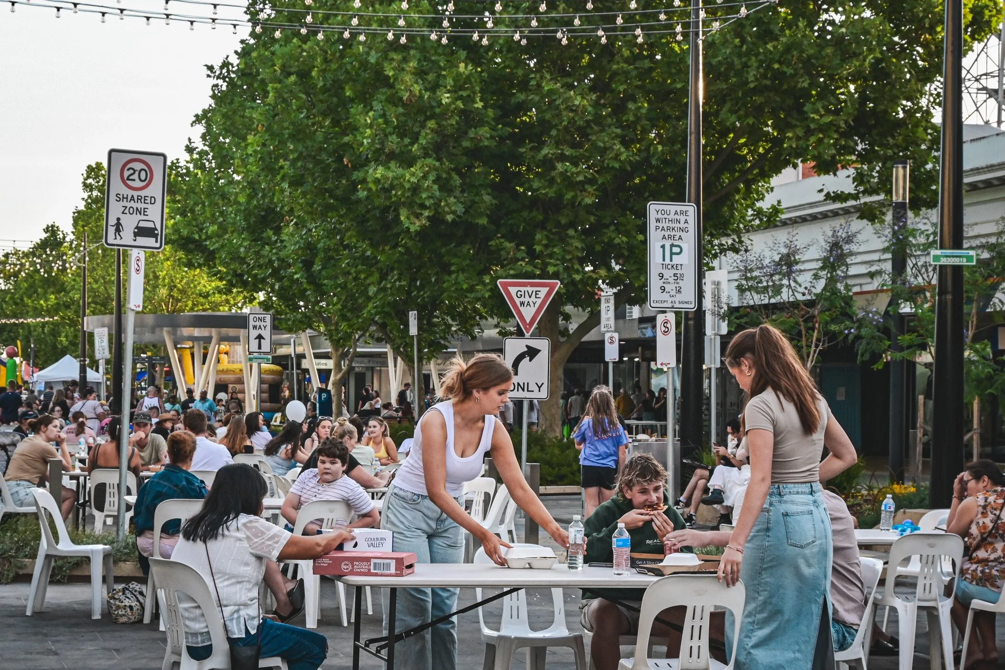 A diverse group of individuals enjoying a meal at outdoor tables during a vibrant food festival.