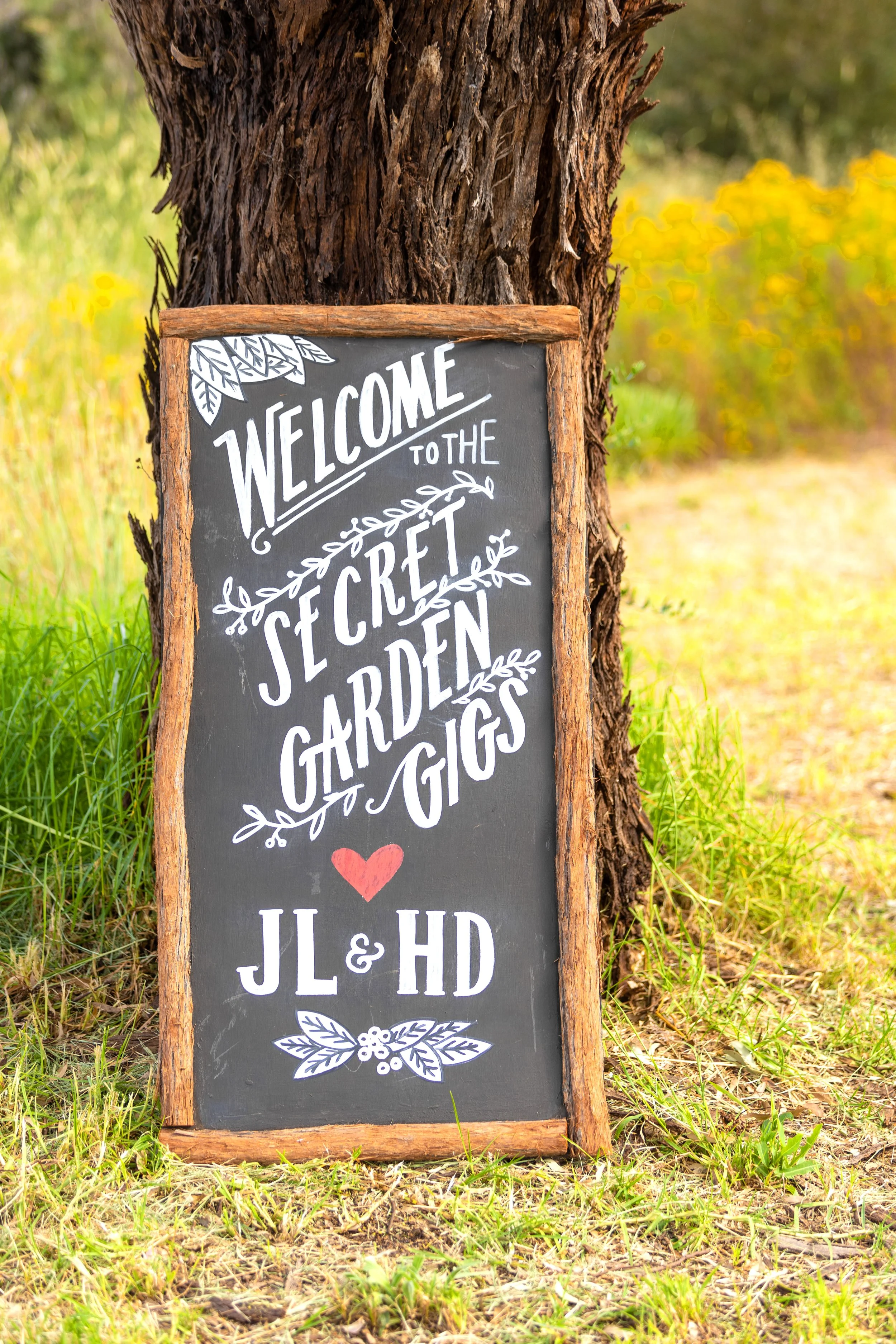 A decorative blackboard sign saying "Welcome to the Secret Garden Gigs, love JL & HD"
