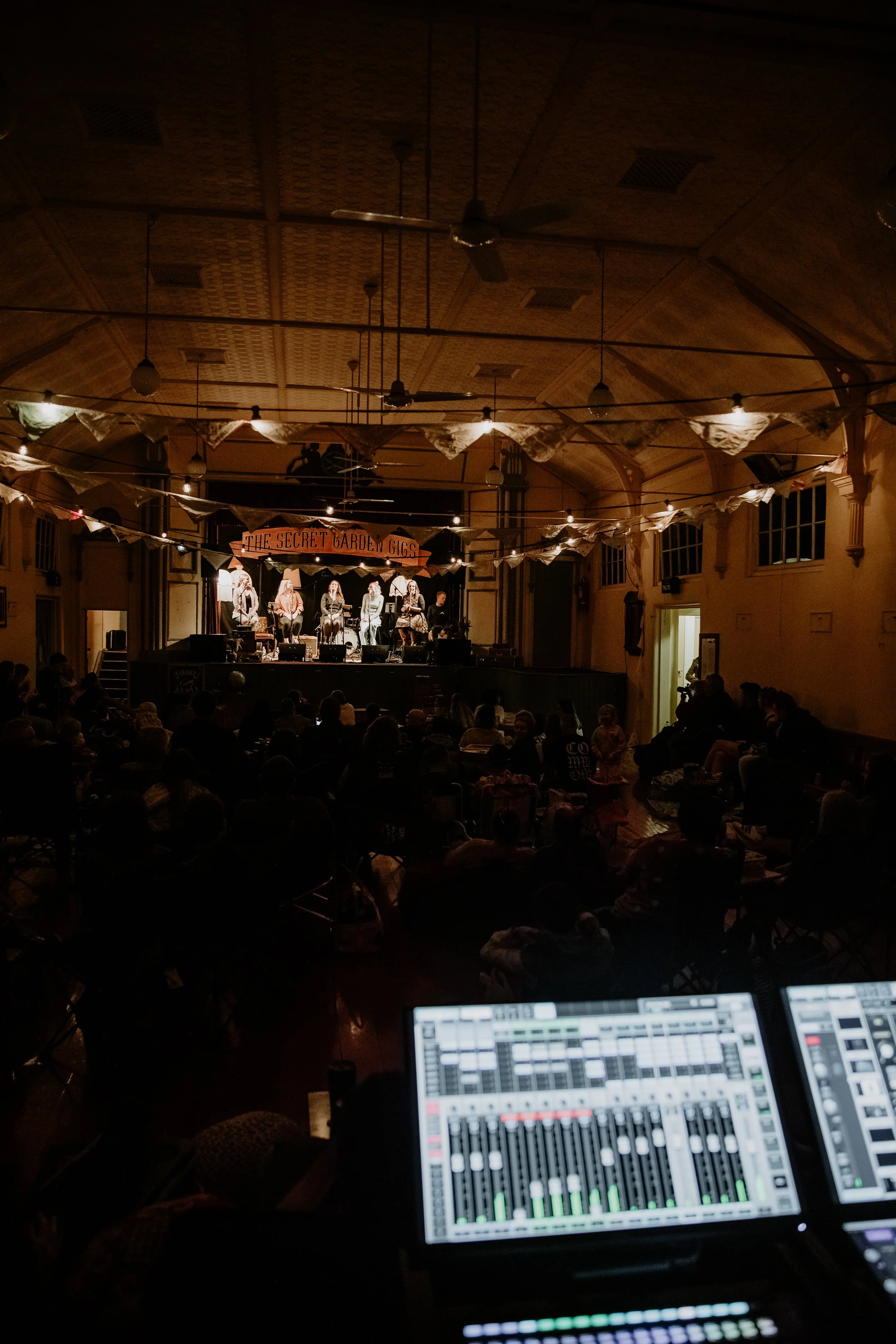 A distant view of the stage with the audio mixers in view.