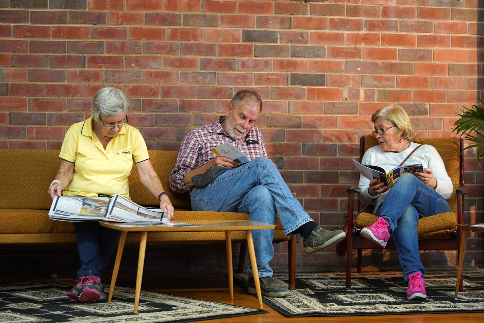 A group of people sitting on vintage chairs, reading and talking.