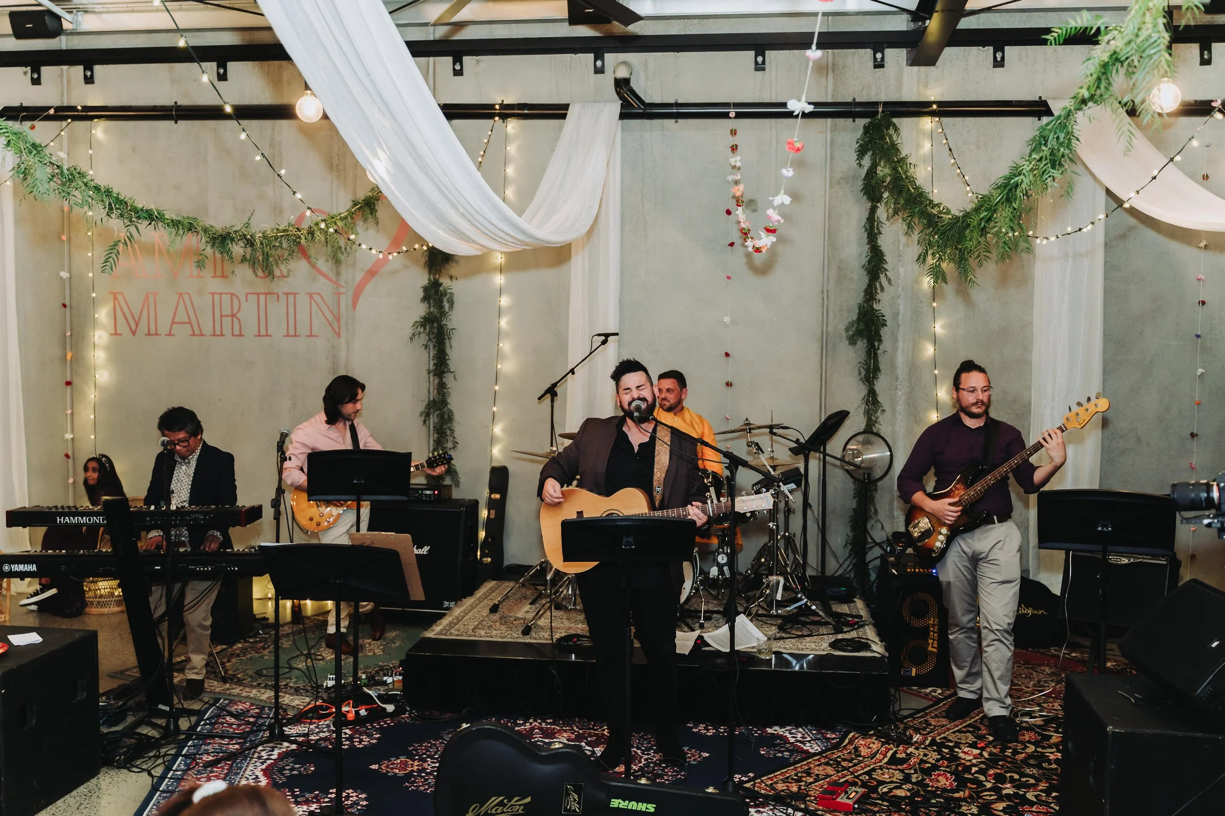 Musicians playing on a spacious stage in a room, with colorful lights and amplifiers creating a vibrant atmosphere.