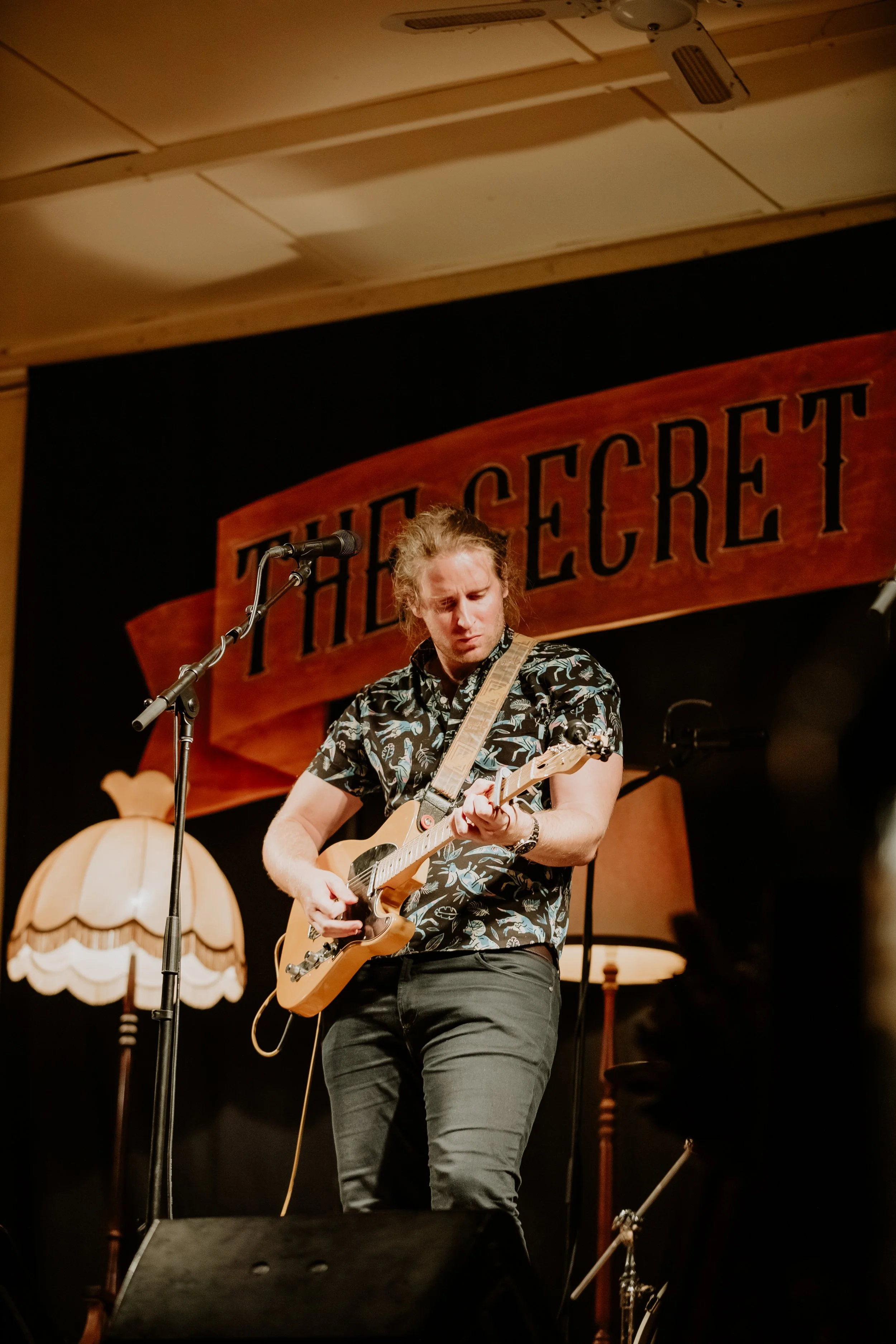 A man playing guitar with vintage style lamps behind him.