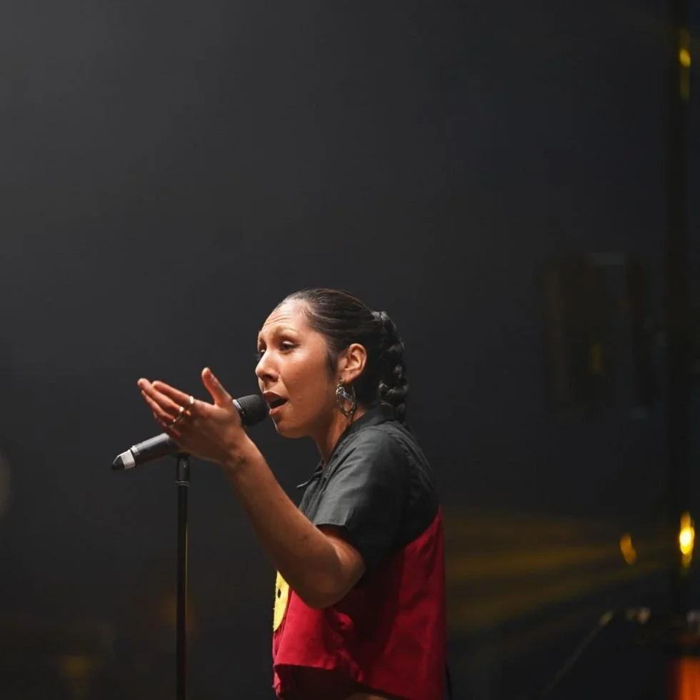 A woman in a red shirt and black pants passionately singing into a microphone at Treaty Day Out.