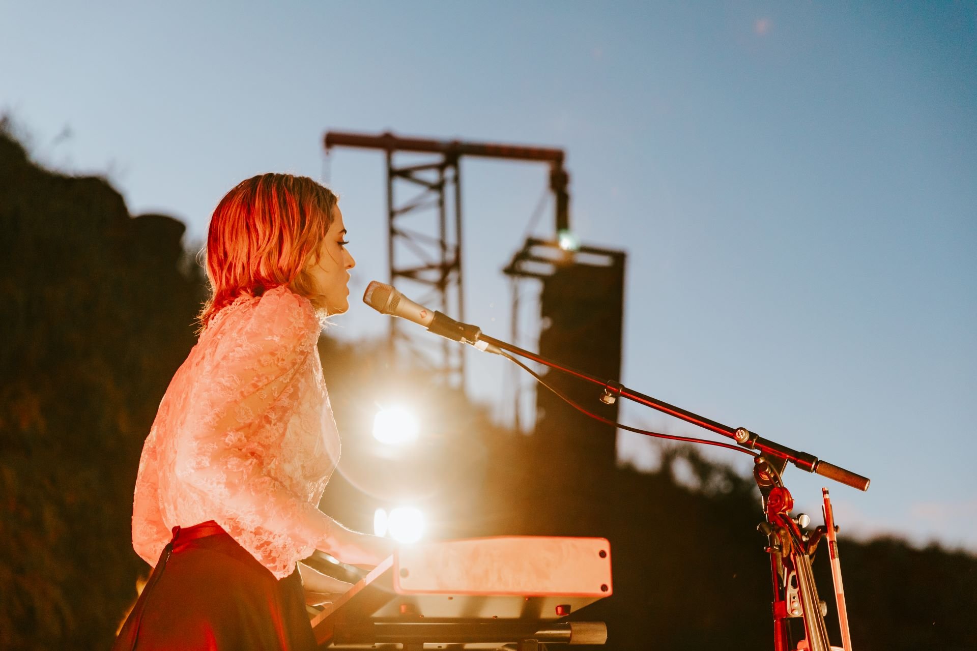 A woman playing a keyboard on stage at sunset during a music festival.