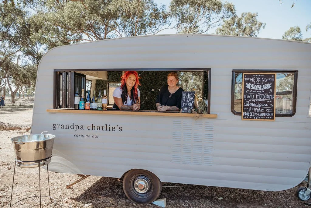 A caravan bar with colorful lights and people enjoying drinks and socializing in an outdoor setting