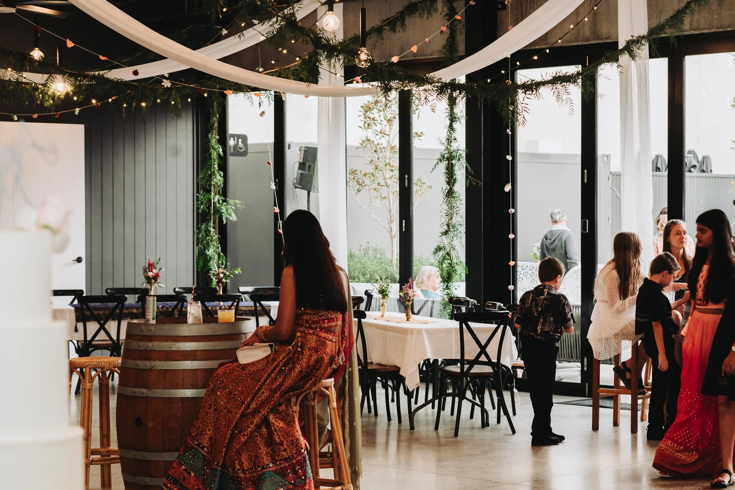 People socialize at a wedding reception, standing near beautifully set tables with floral arrangements.