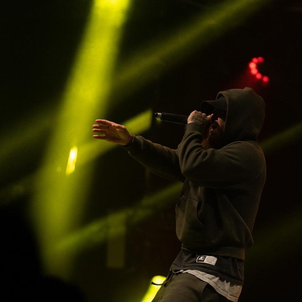 Nooky in hoodie raising hands on stage during Treaty Day Out celebration.