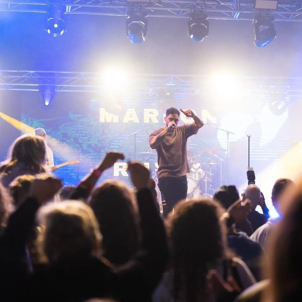 A man on stage with his hands raised in celebration during the Treaty Day Out event as part of Marlon x Rulla set.