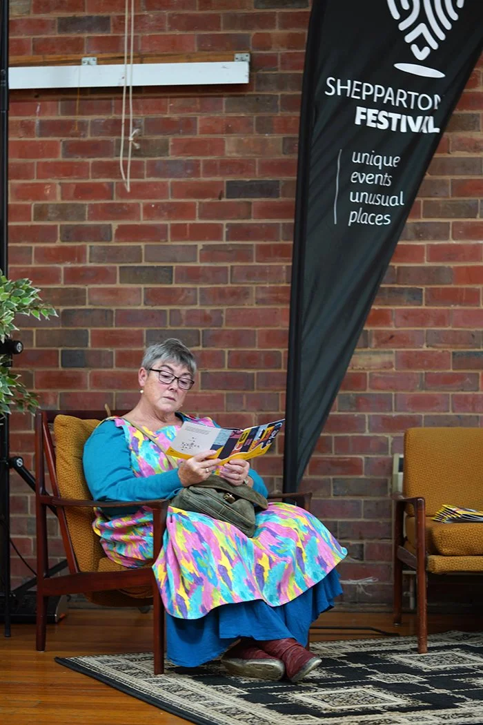 A woman in bright colours, sits thoughtfully reading.