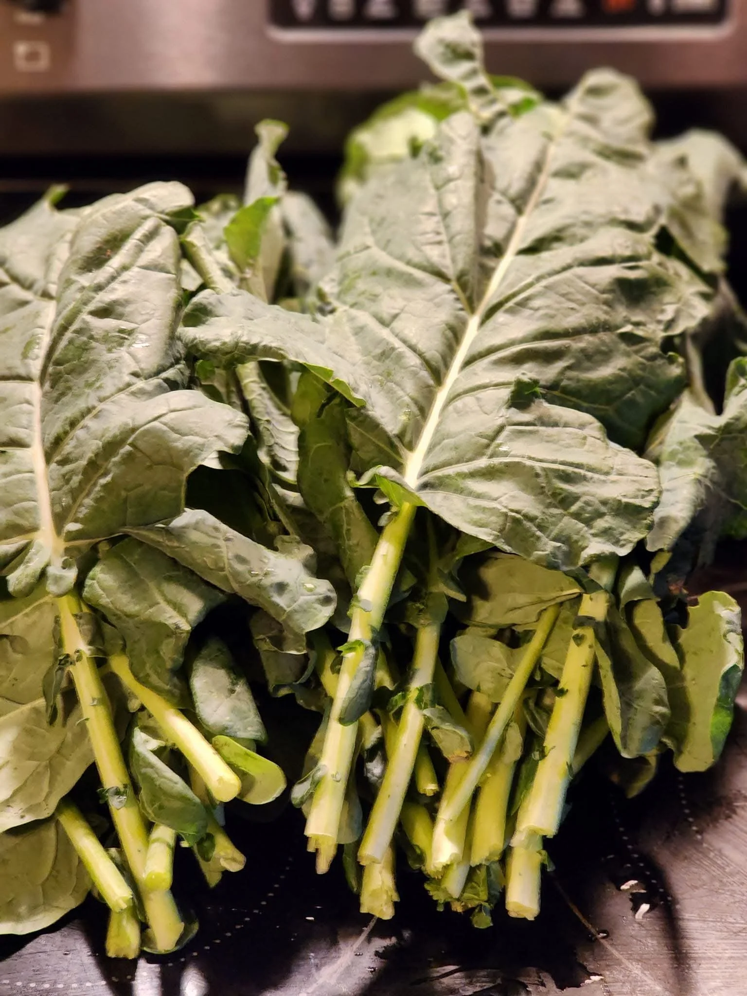 A bunch of fresh, leafy greens with thick stems, likely Swiss chard, on a dark surface.
