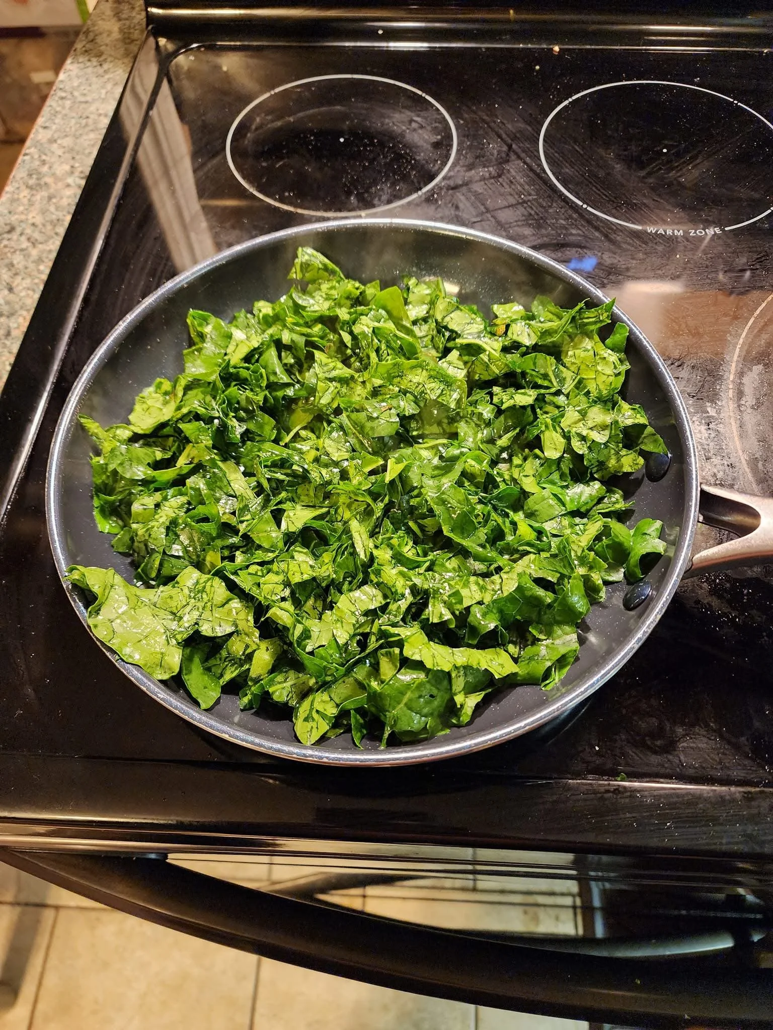 Chopped leafy greens in a frying pan on a black stove.