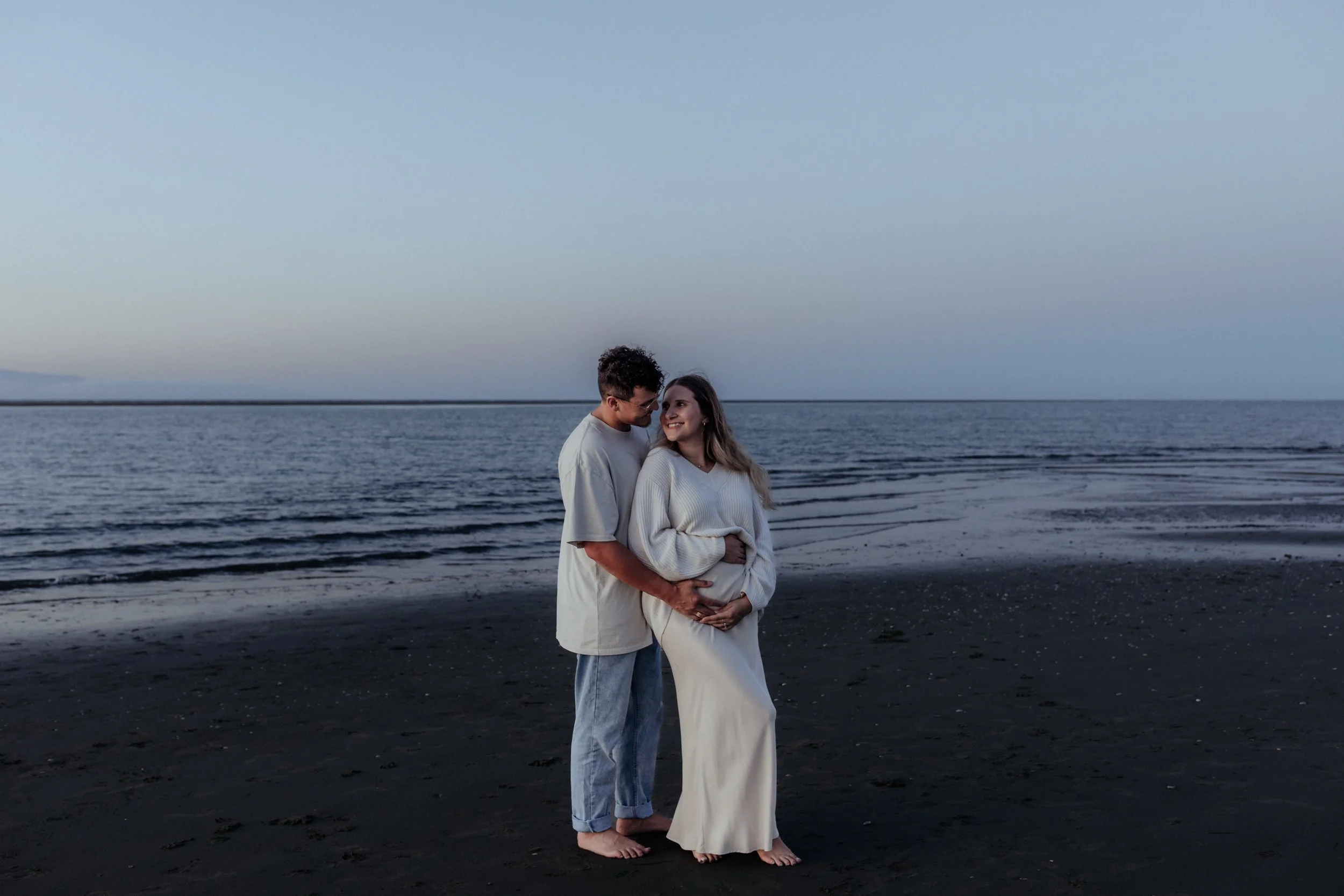 Couple embracing during sunset maternity session at beach.