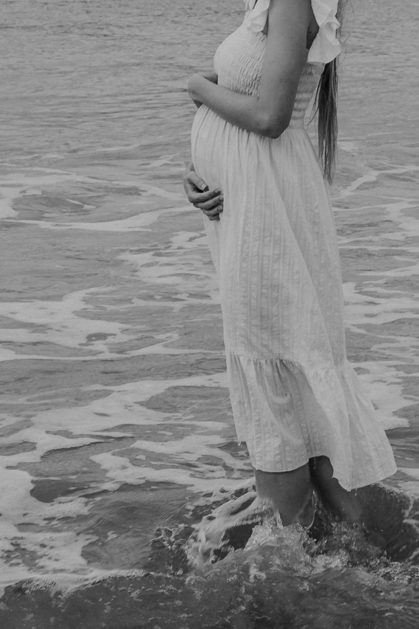 Pregnant women wades in water at the beach during Whangarei maternity photoshoot.