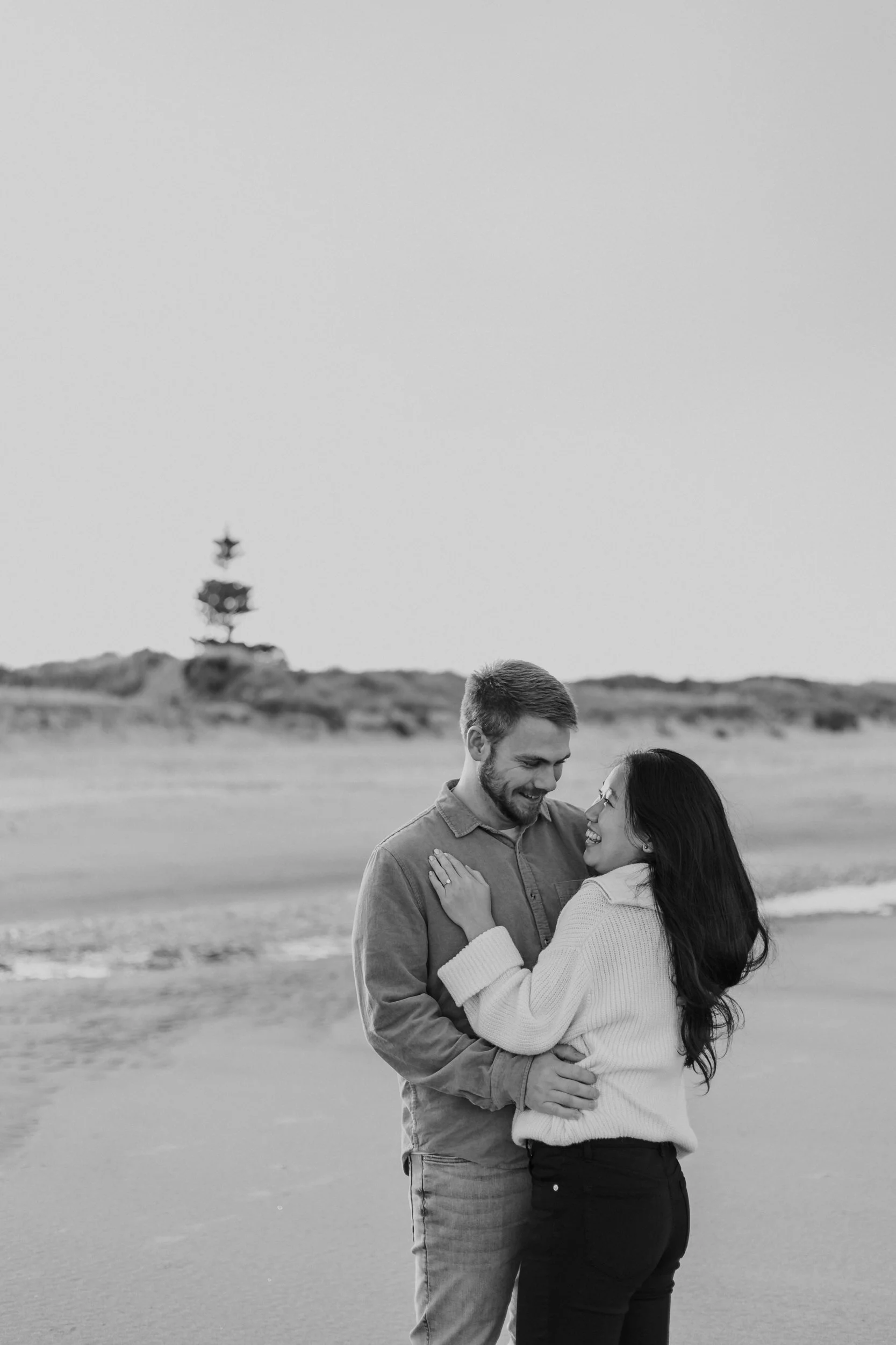 Newly engaged couple embracing at Northland beach during photoshoot at golden hour.