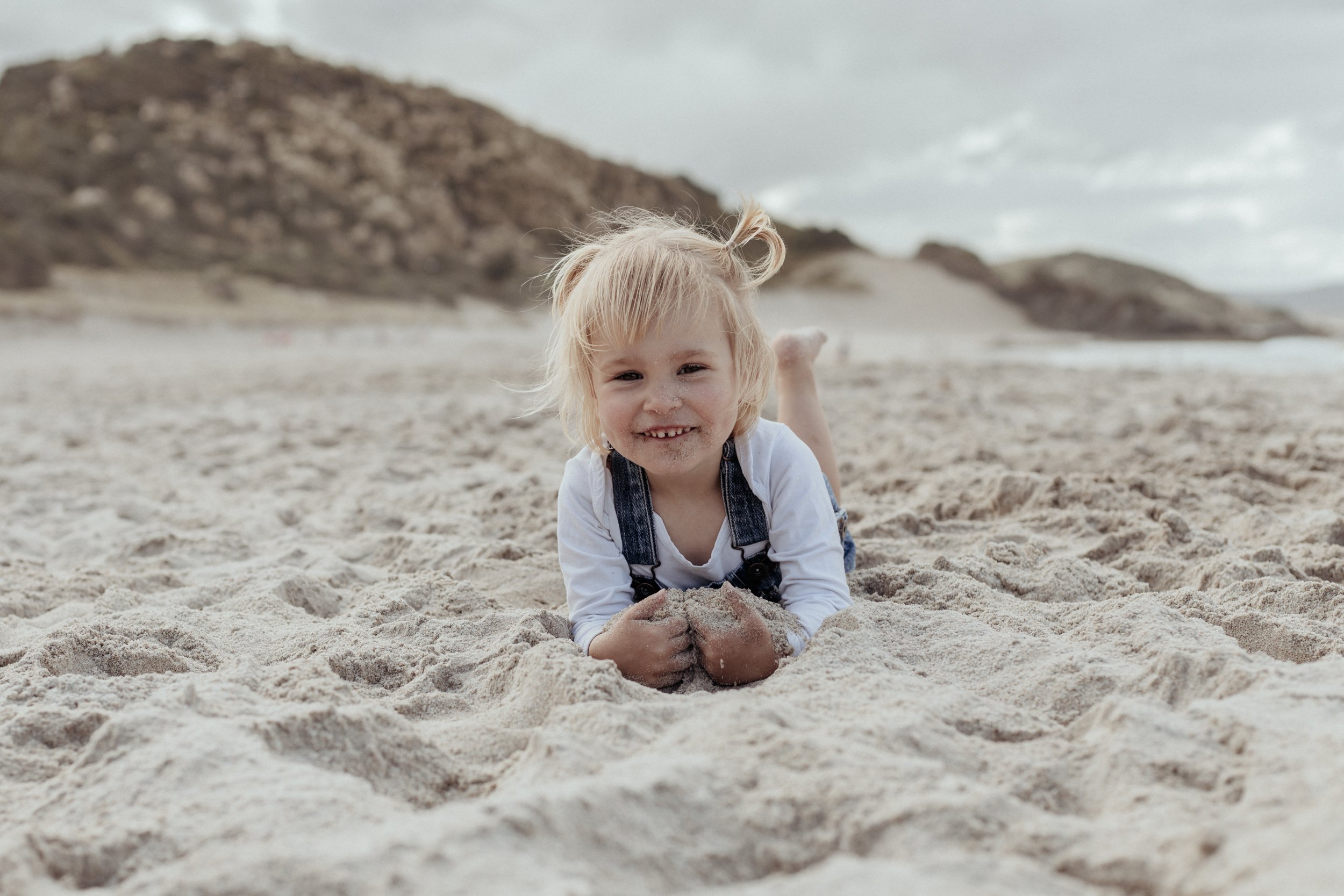 Child plays in sand at family photoshoot at Whangarei beach.