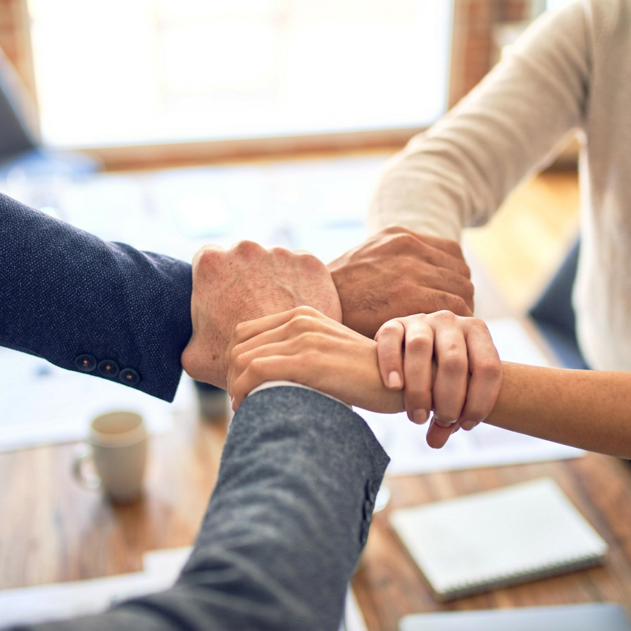 Four people holding hands together in a team unity gesture, viewed from above.