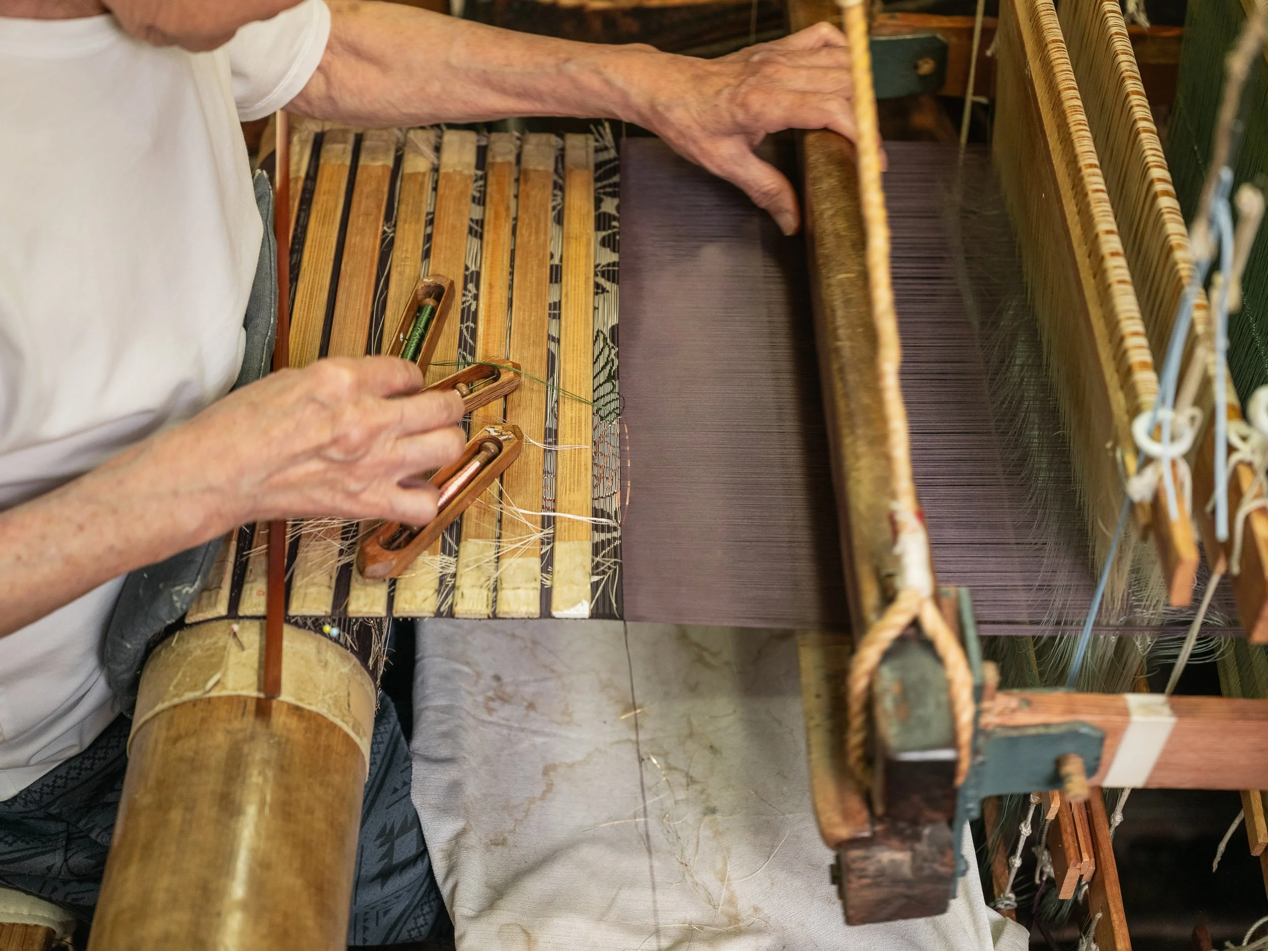 An employee works at a loom in a workshop producing costumes for Noh theatre.