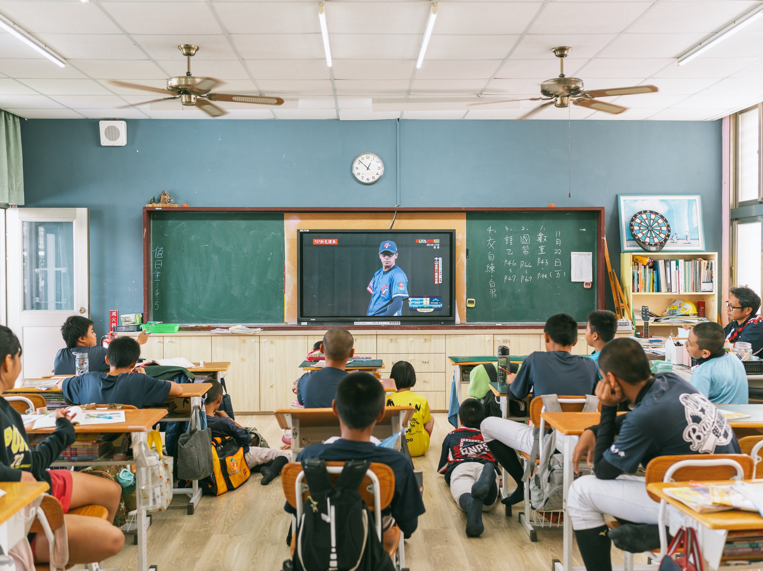 The 6th-grade sports program students (including members of Team A) are taking advantage of their lunch break to watch the Premium12 baseball game between Taiwan and the USA at Bei-Nan Elementary School in Taitung.