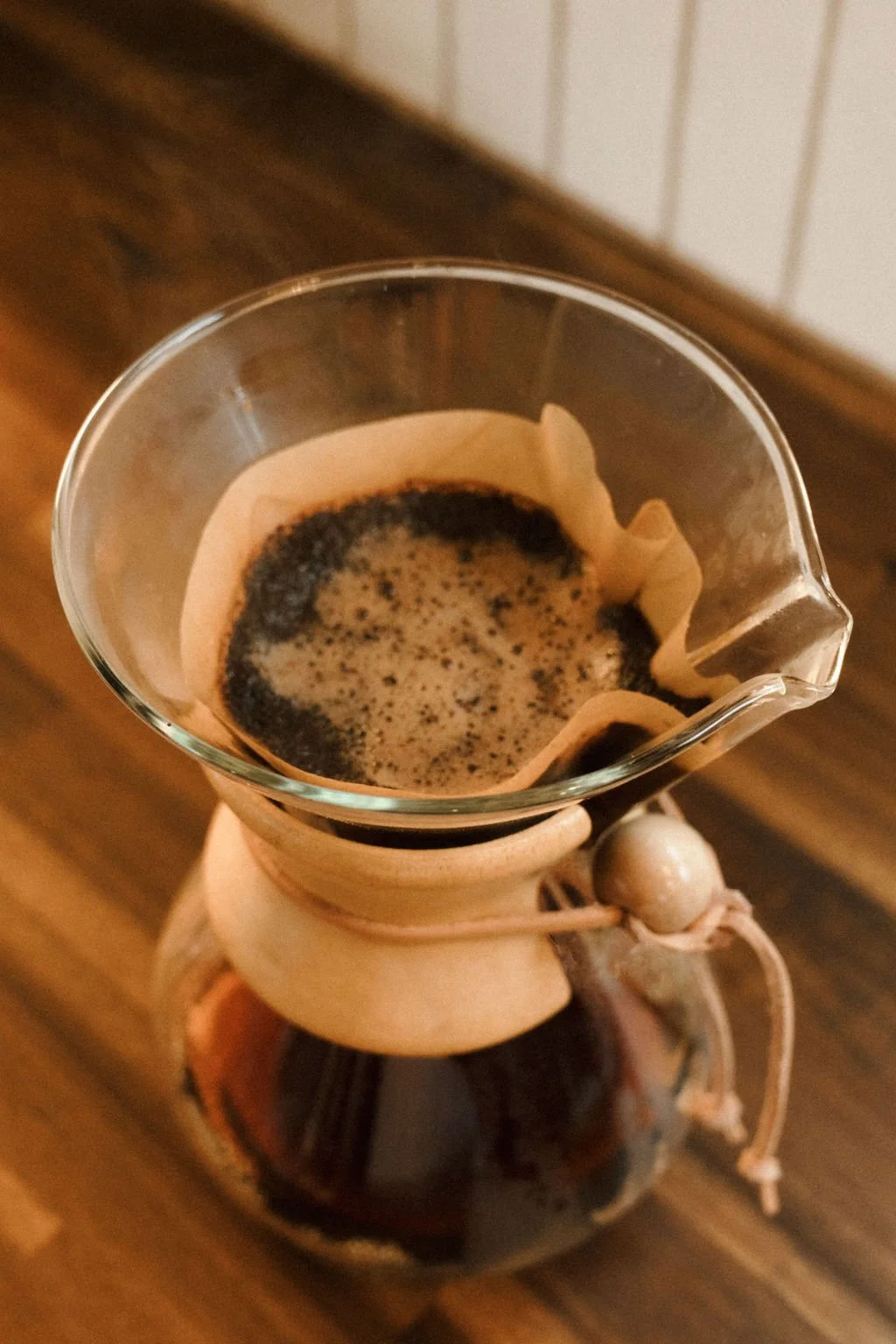 Pour-over coffee brewing in a glass cup with a paper filter, placed on a wooden table.