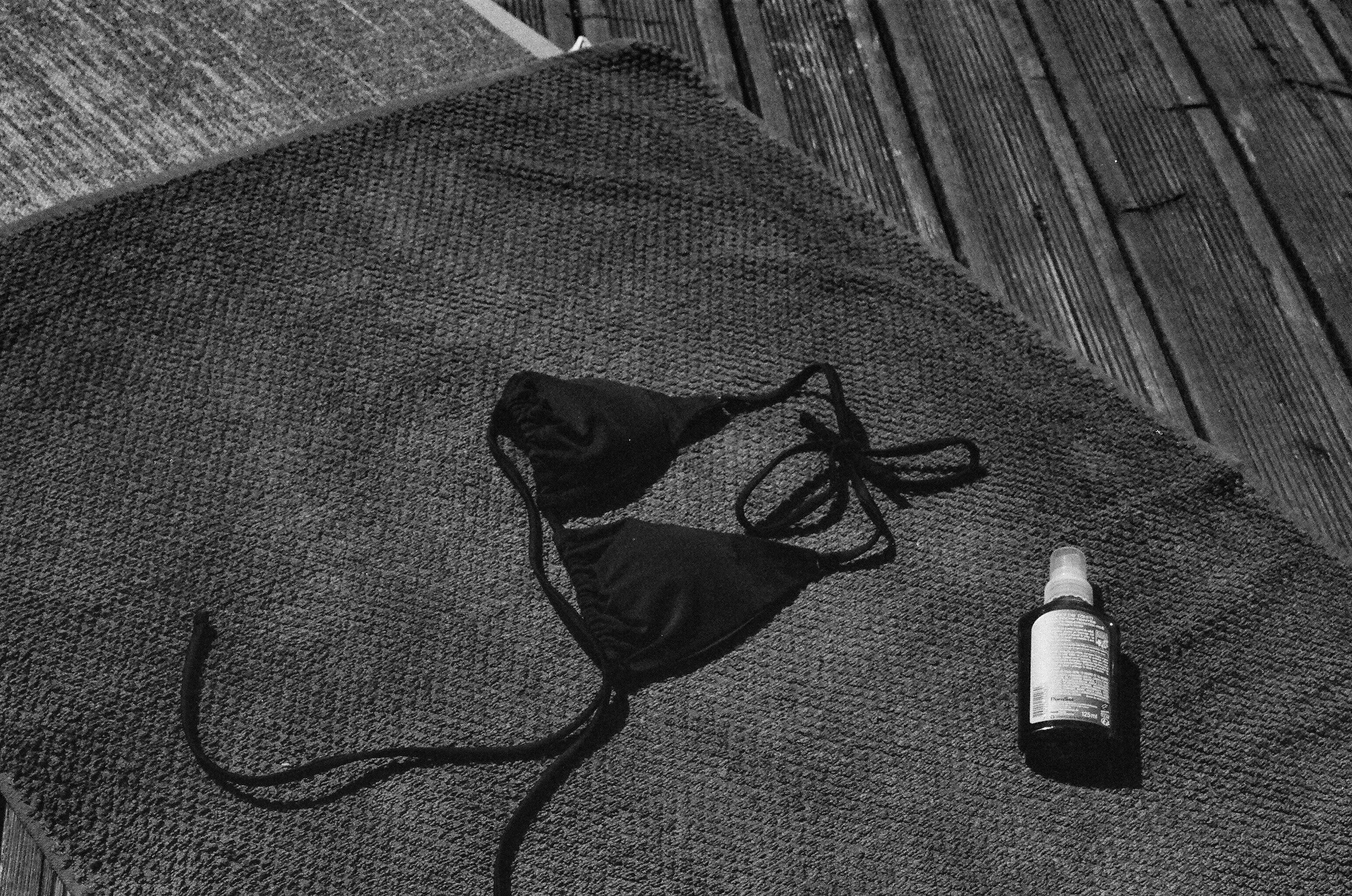 A black face mask and a small bottle of spray sanitizer on a textured fabric surface, near a wooden floor.