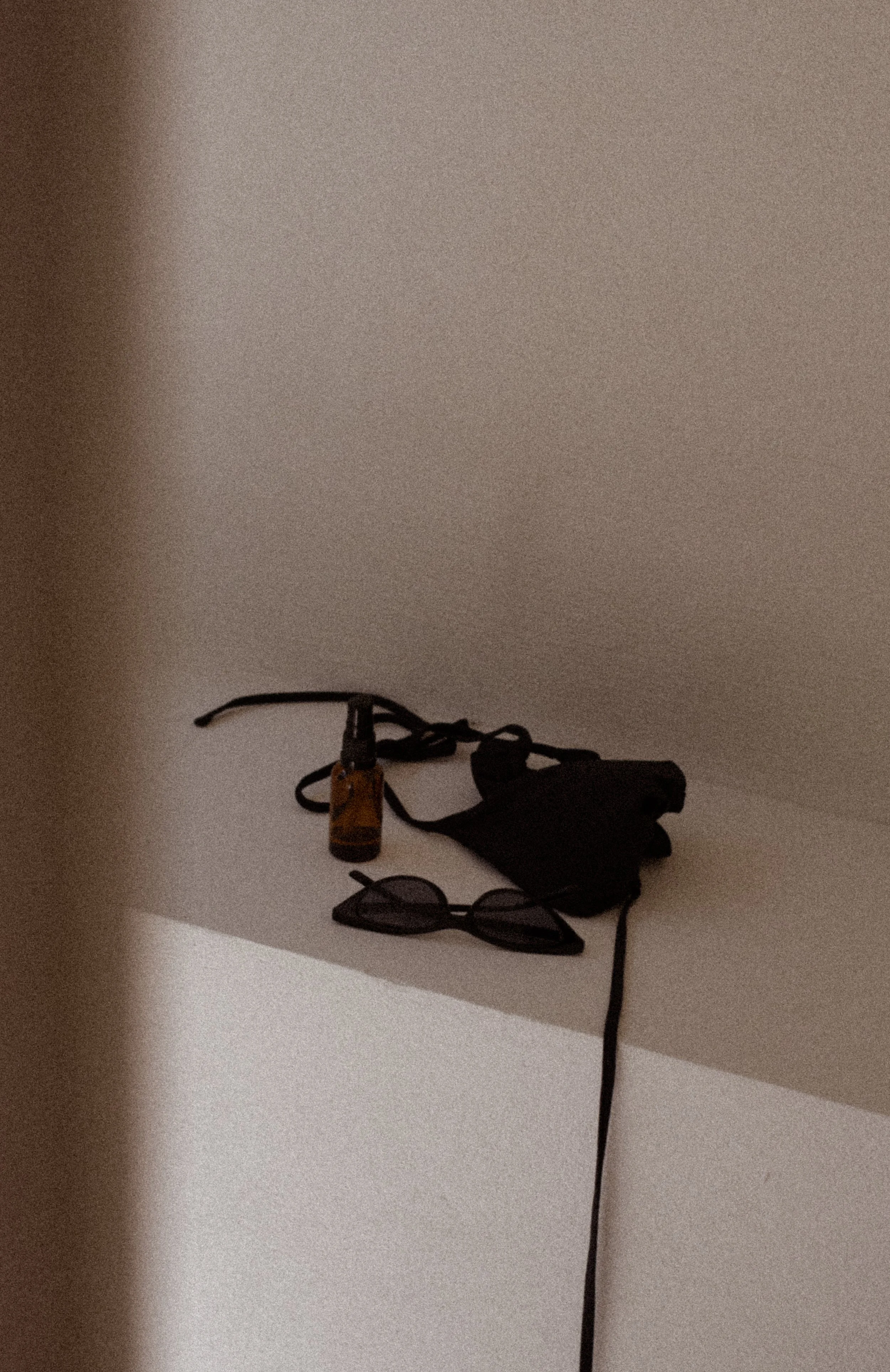 Personal items on a white surface including sunglasses, a mask, a small bottle, and cords