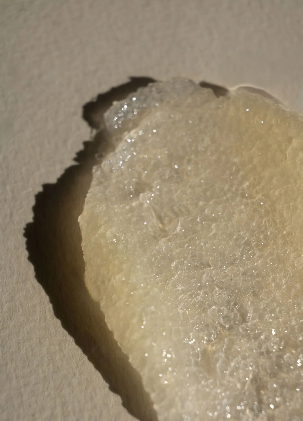 Close-up of a large, translucent, textured soap slice on a beige surface with a small hole in the background.