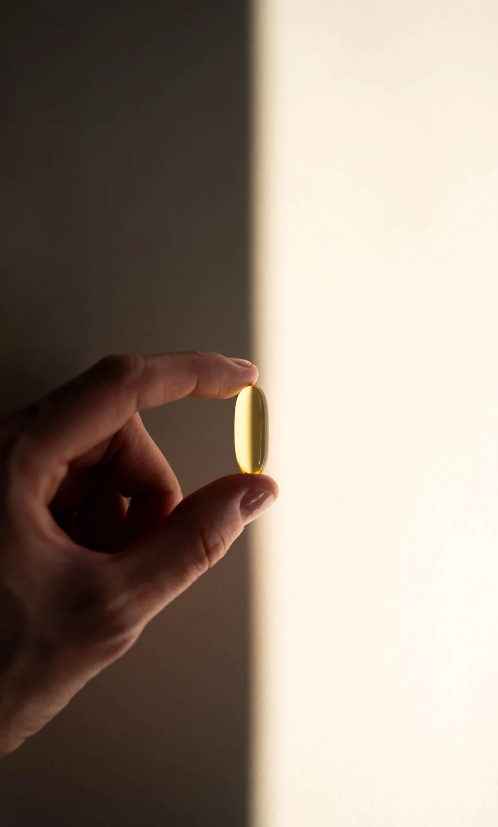A hand holding a yellow capsule-shaped supplement or medication with a light-colored background.